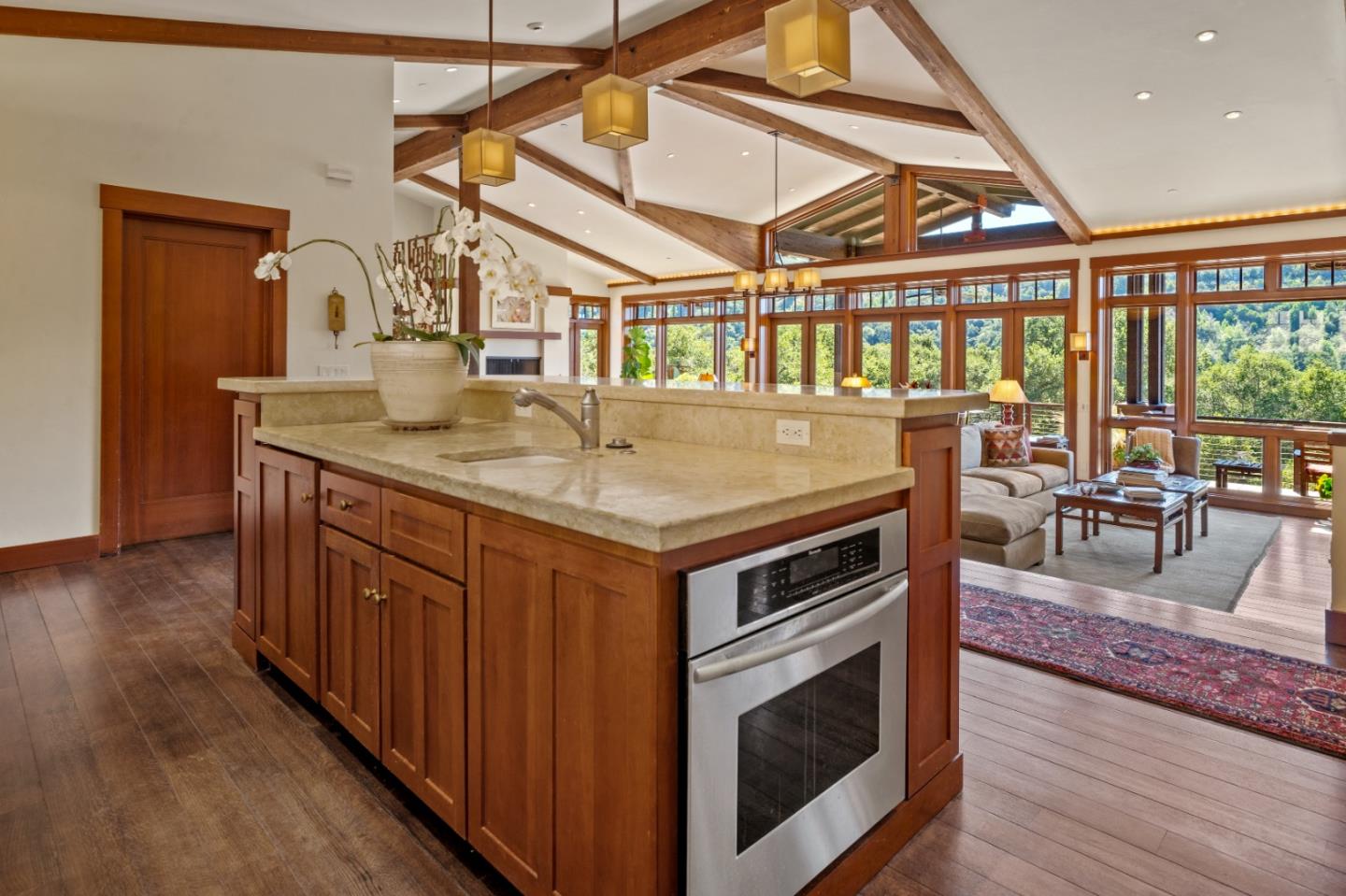 Kitchen with a large wood island, exposed ceiling beams, and windows overlooking wooded hills.