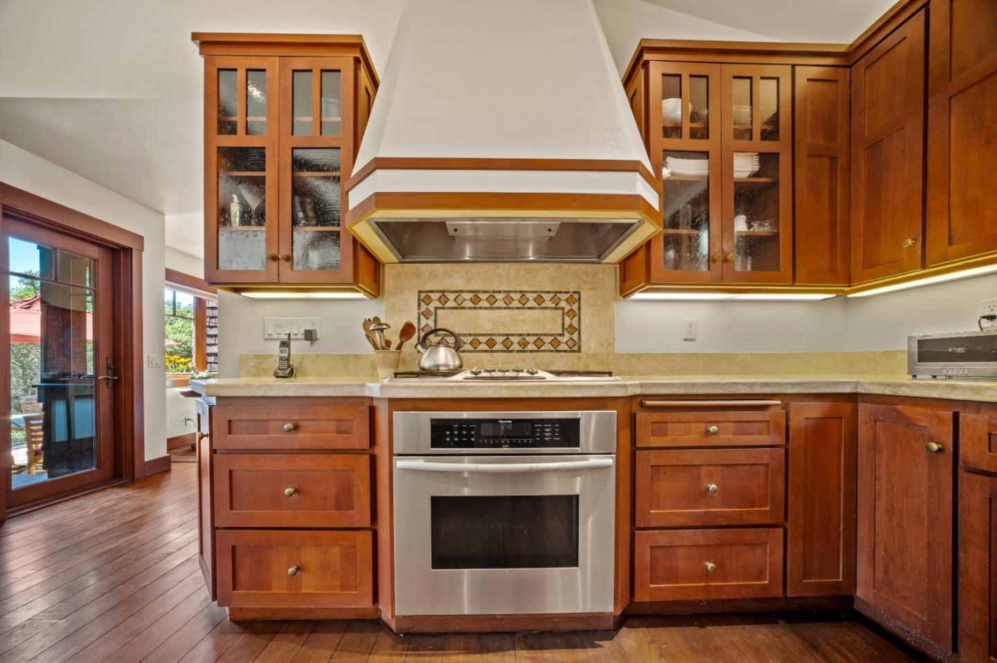 Kitchen with rich wood cabinets, a stainless steel oven, and a large white range hood.