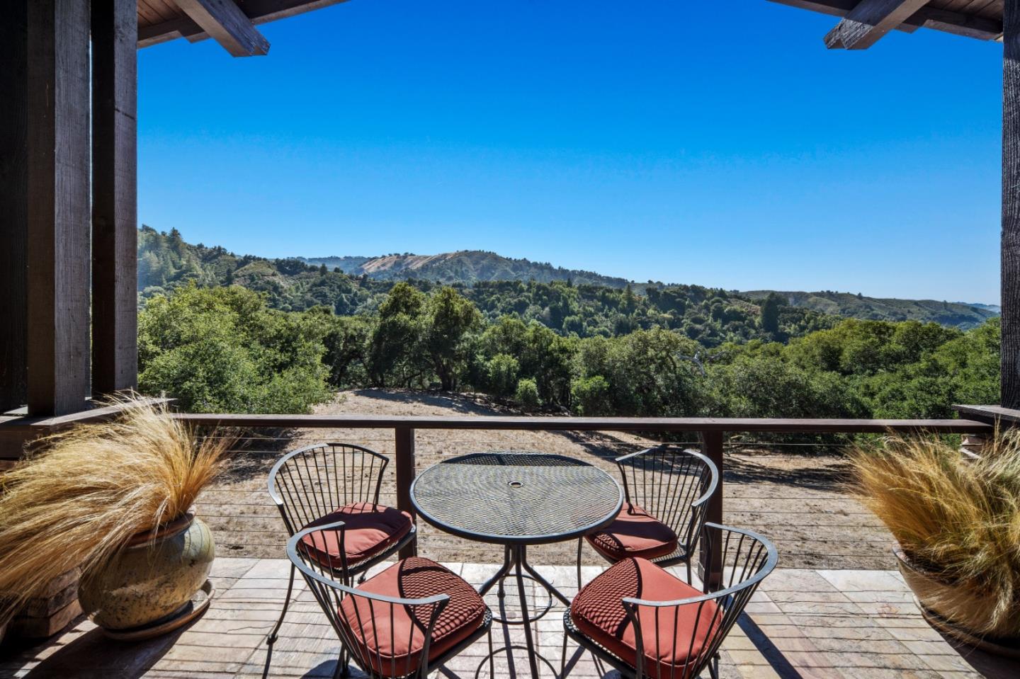 Patio seating overlooks wooded hills from beneath a timber-covered structure.