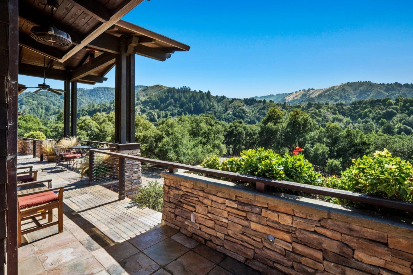 Covered stone patio with outdoor seating overlooking wooded hills.