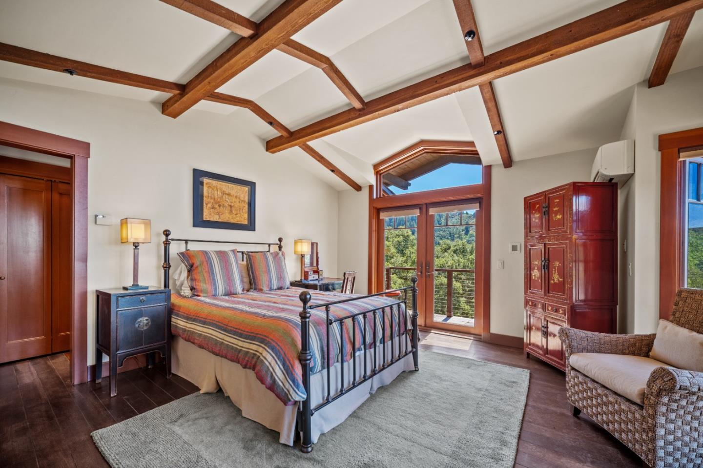 Bedroom with exposed wood beams, a striped quilt, and glass doors overlooking trees.