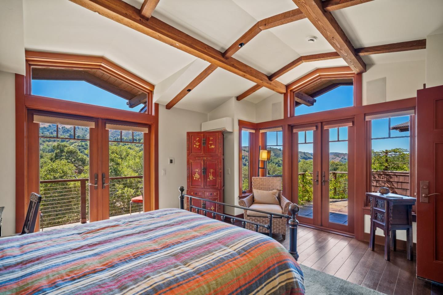 Bedroom with exposed timber beams and large windows overlooking wooded hills.