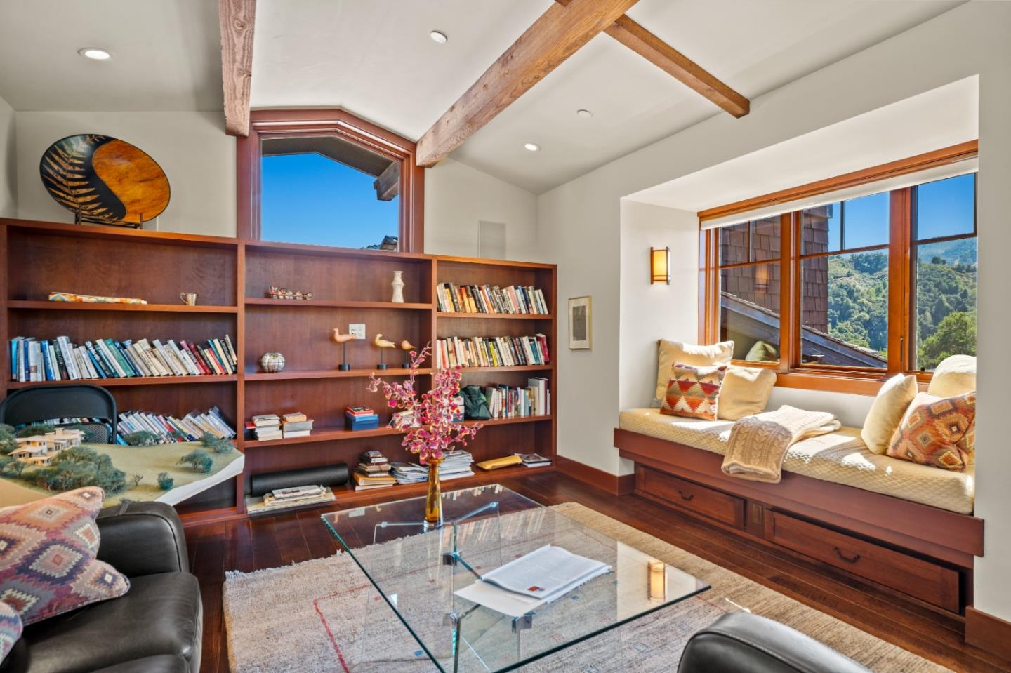 Library with built-in bookshelves, a window seat, exposed beams, and wooded hill views.