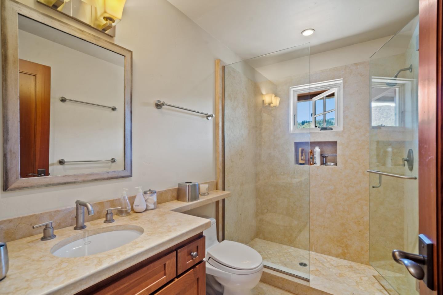 Bathroom with a beige stone vanity, wood cabinetry, and glass-enclosed shower.