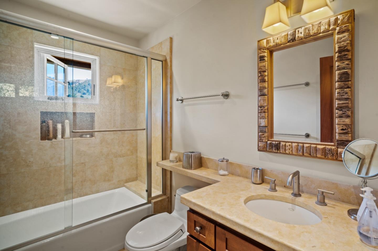 Bathroom with a glass-enclosed tub and shower, stone tile, and a large wood-framed mirror.