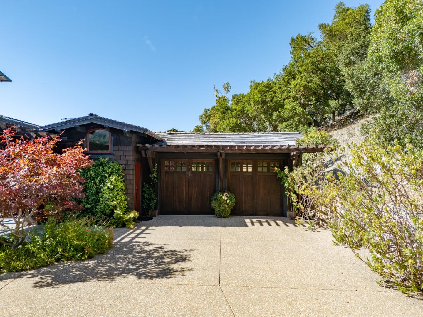 Dark wood home with double garage and timber pergola, framed by trees and landscaping.