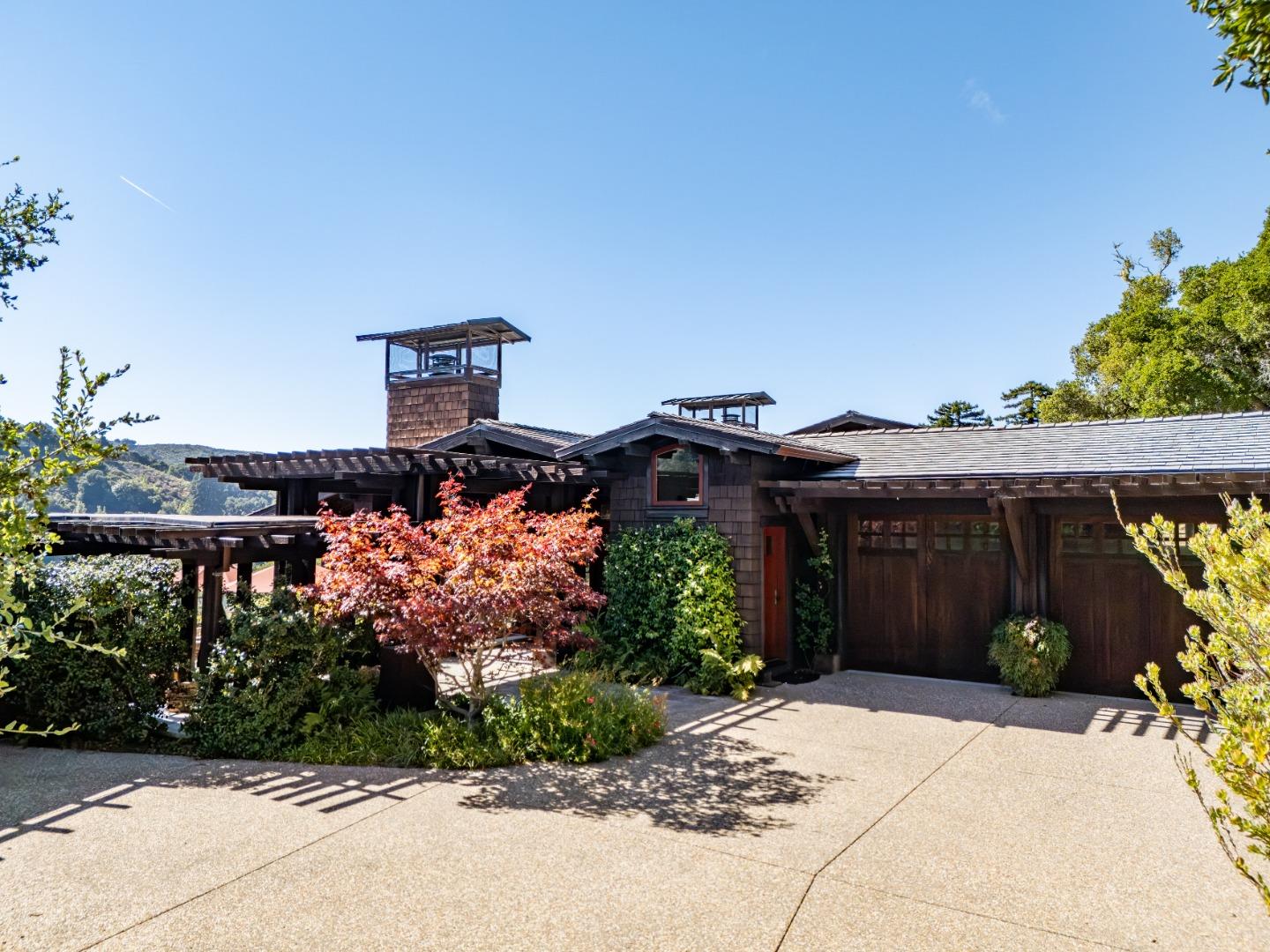 Dark shingled home with rooftop cupolas, covered parking, and a red-leaved Japanese maple by the driveway.