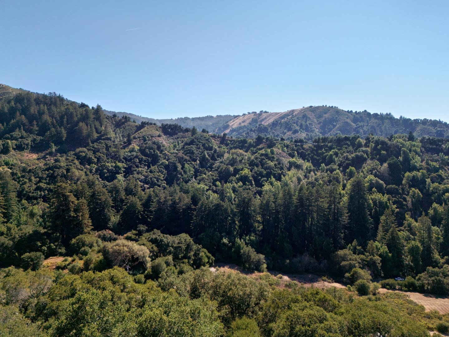 Aerial view of a wooded valley and rolling hills beneath a clear blue sky.