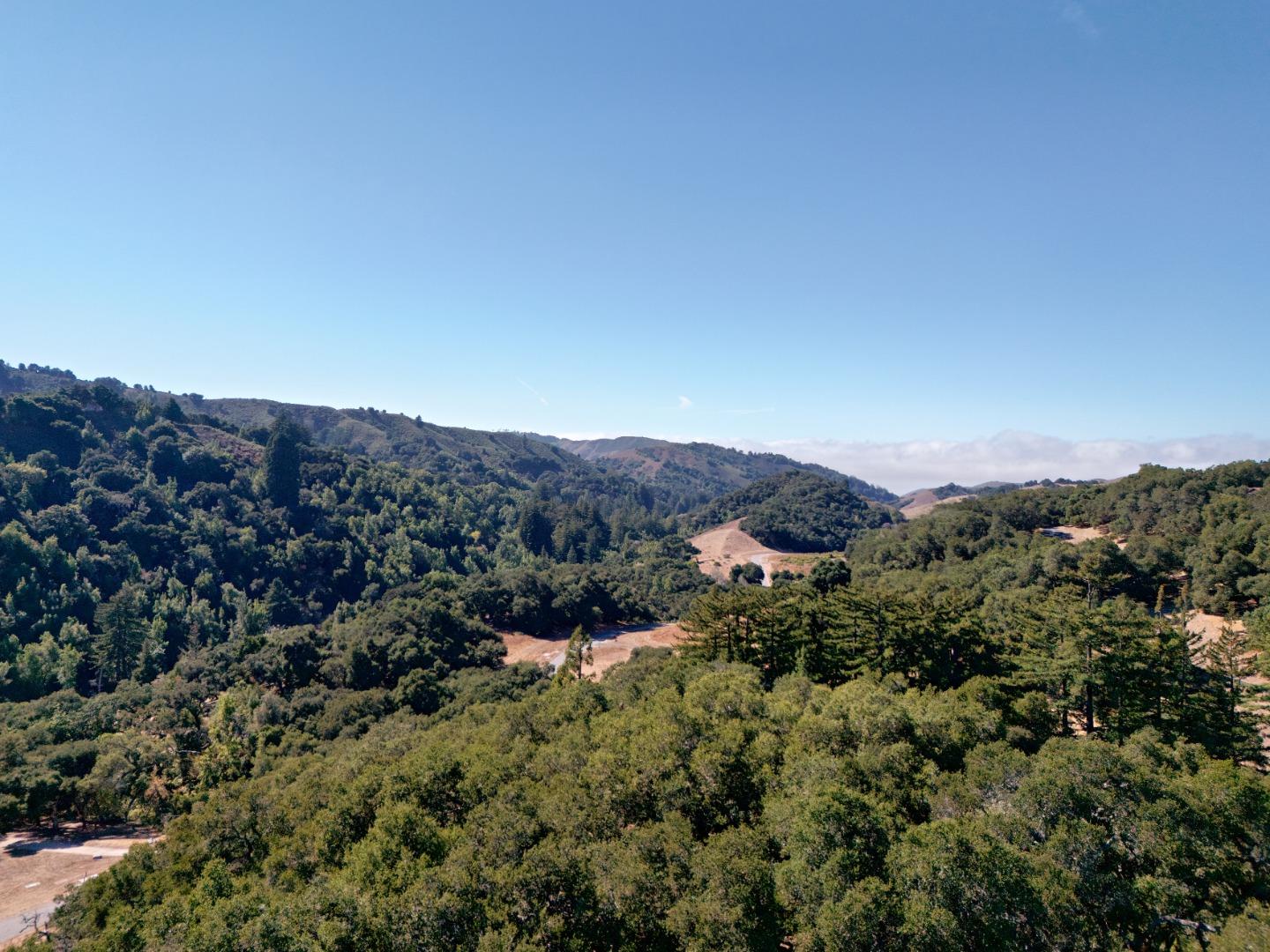 Aerial view of wooded rolling hills and valley with several open clearings.