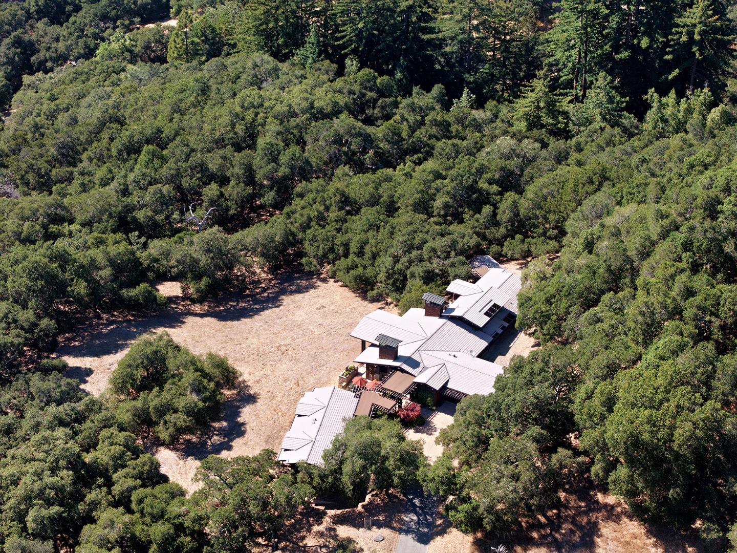 Aerial view of a large, multi-roofed home in a woodland clearing.