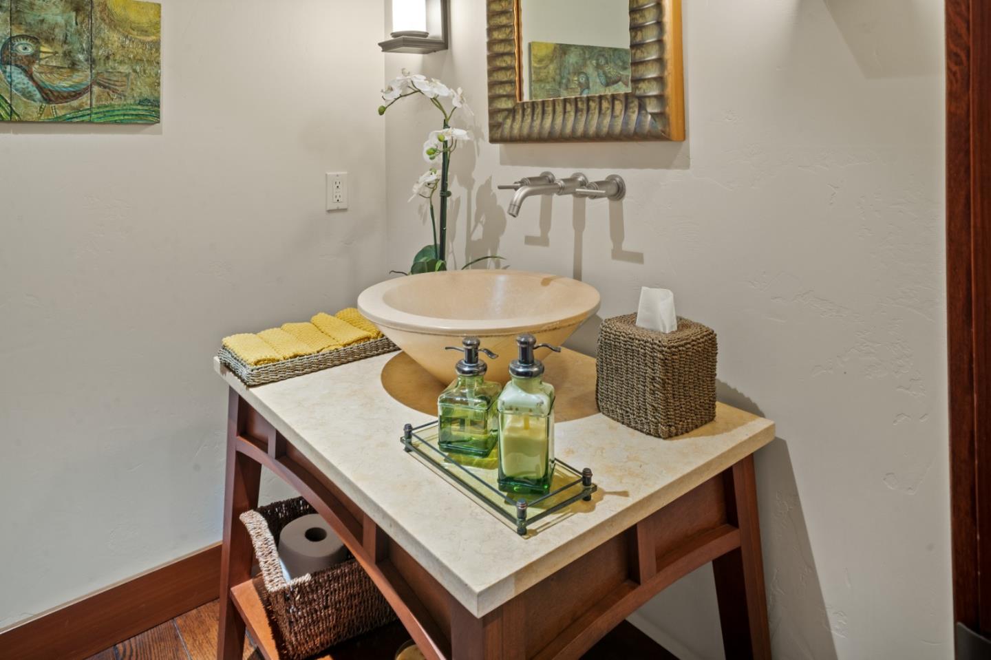 Bathroom vanity with a cream vessel sink, stone countertop, wall-mounted faucet, and wood cabinetry.