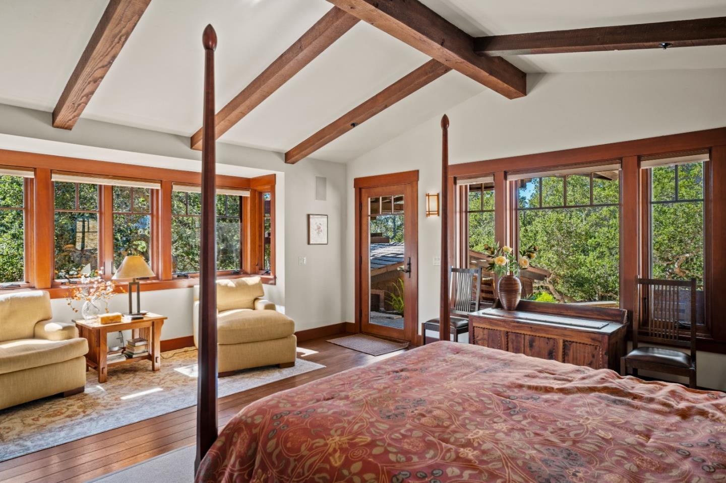Bedroom with exposed timber beams, a patterned bedspread, and large windows overlooking greenery.