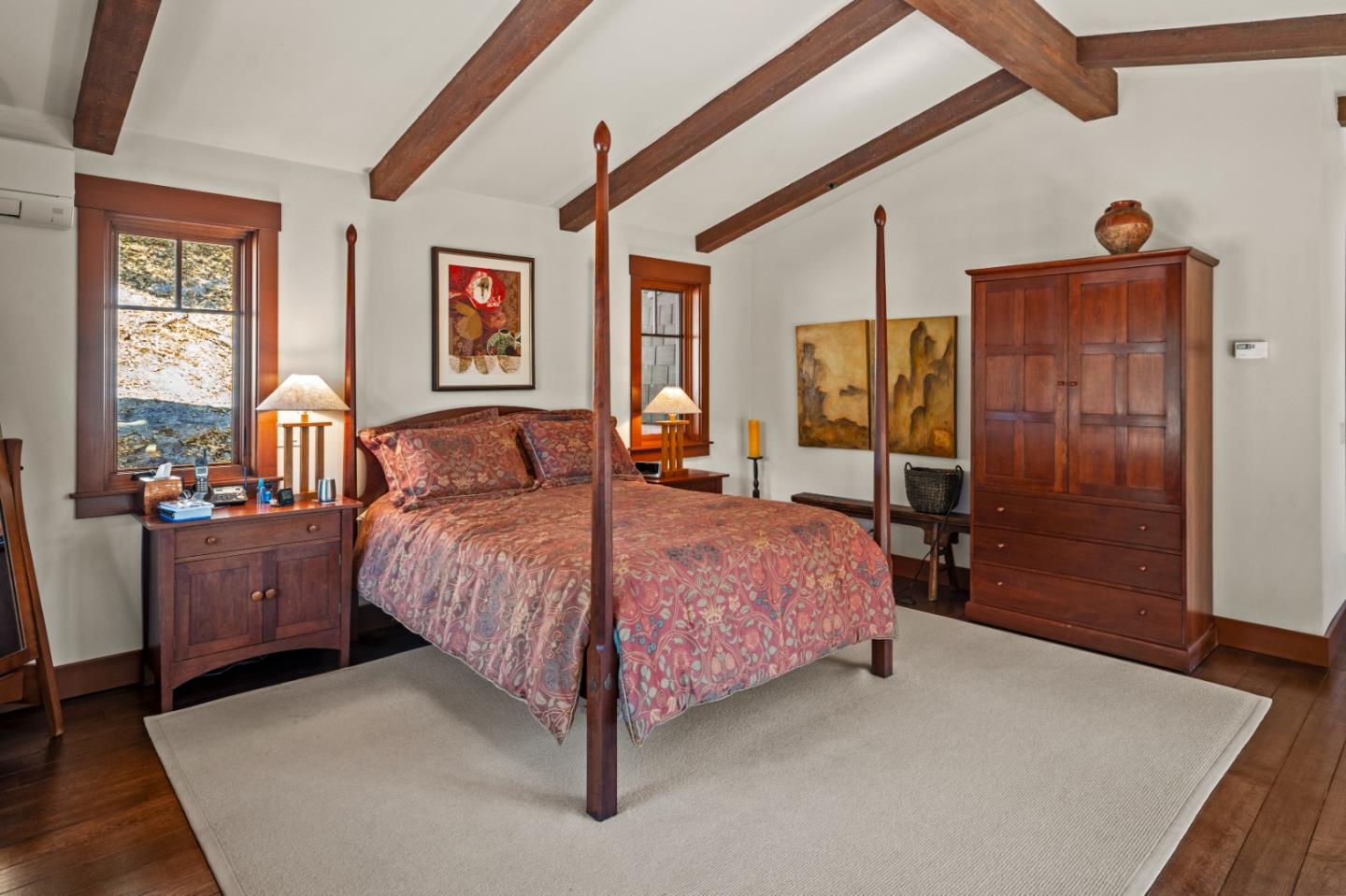 Bedroom with a four-poster bed, patterned quilt, exposed wood beams, and matching wooden furniture.