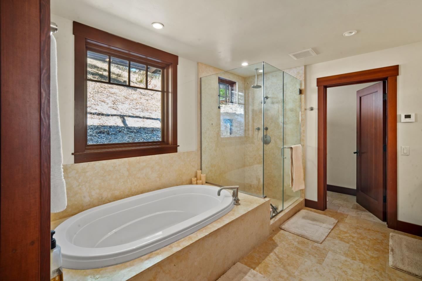 Bathroom with an oval soaking tub beside a glass-enclosed shower and a large hillside-facing window.