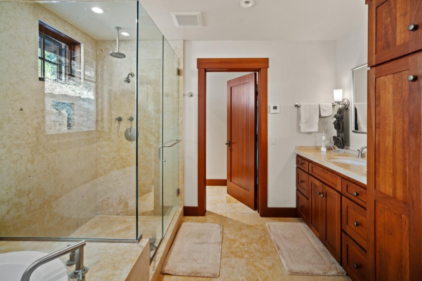 Bathroom with a glass-enclosed beige stone shower and a long dark wood vanity.