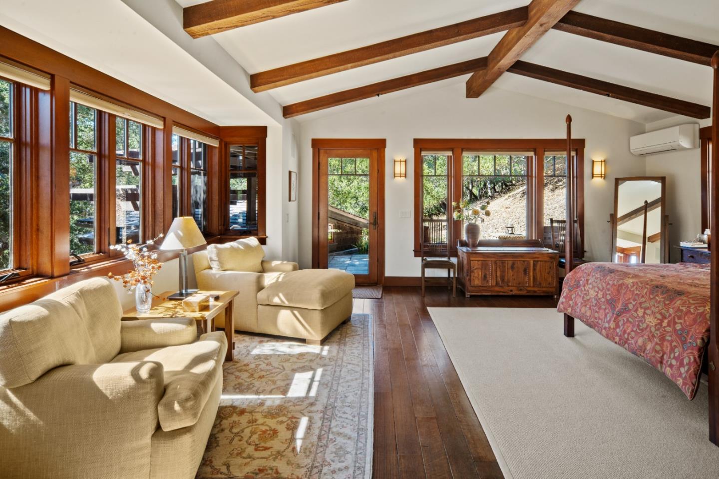 Bedroom with exposed wood beams, large windows, hardwood floors, and a furnished sitting area.