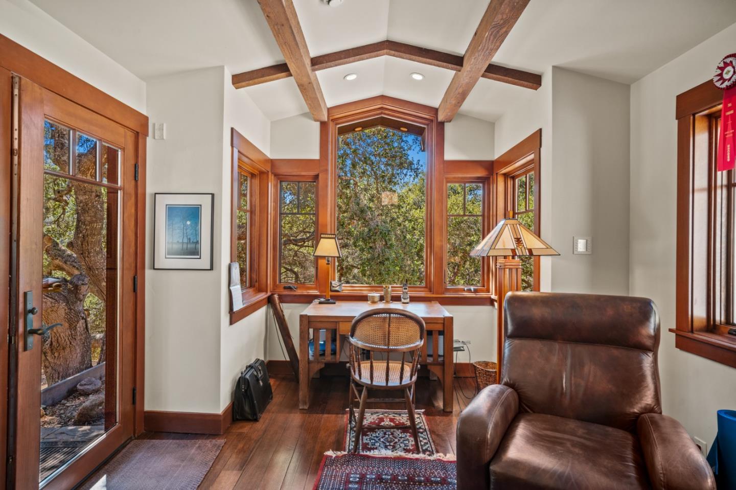 Furnished study with exposed ceiling beams, wood-trimmed windows, and a leather armchair.