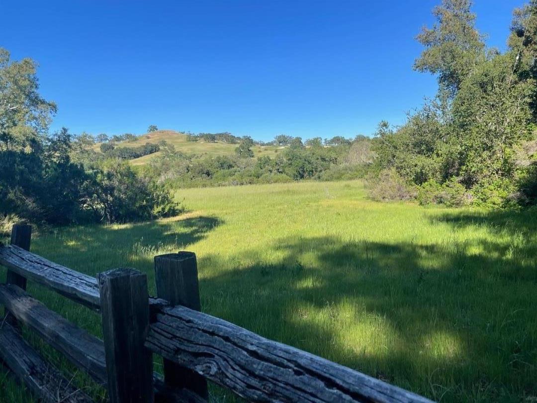 Grassy meadow with a weathered wooden fence and rolling hills beyond.