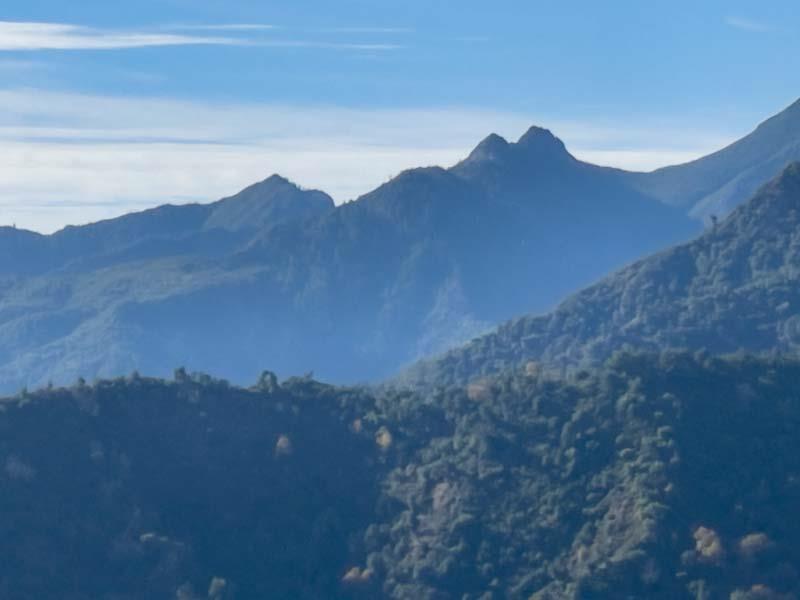Mountain range with forested ridges beneath a blue, lightly clouded sky.