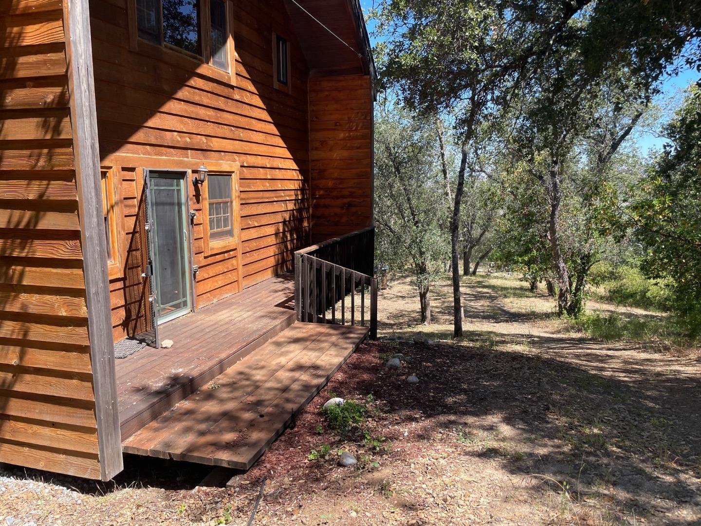 Wood-sided cabin with a raised deck overlooking a wooded yard.
