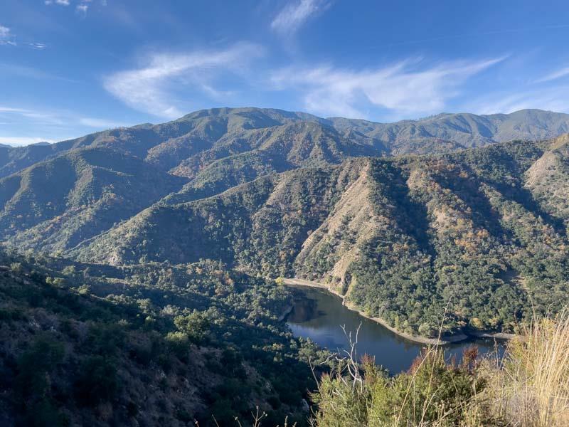Mountain and reservoir view from an elevated hillside, with wooded slopes and autumn foliage.
