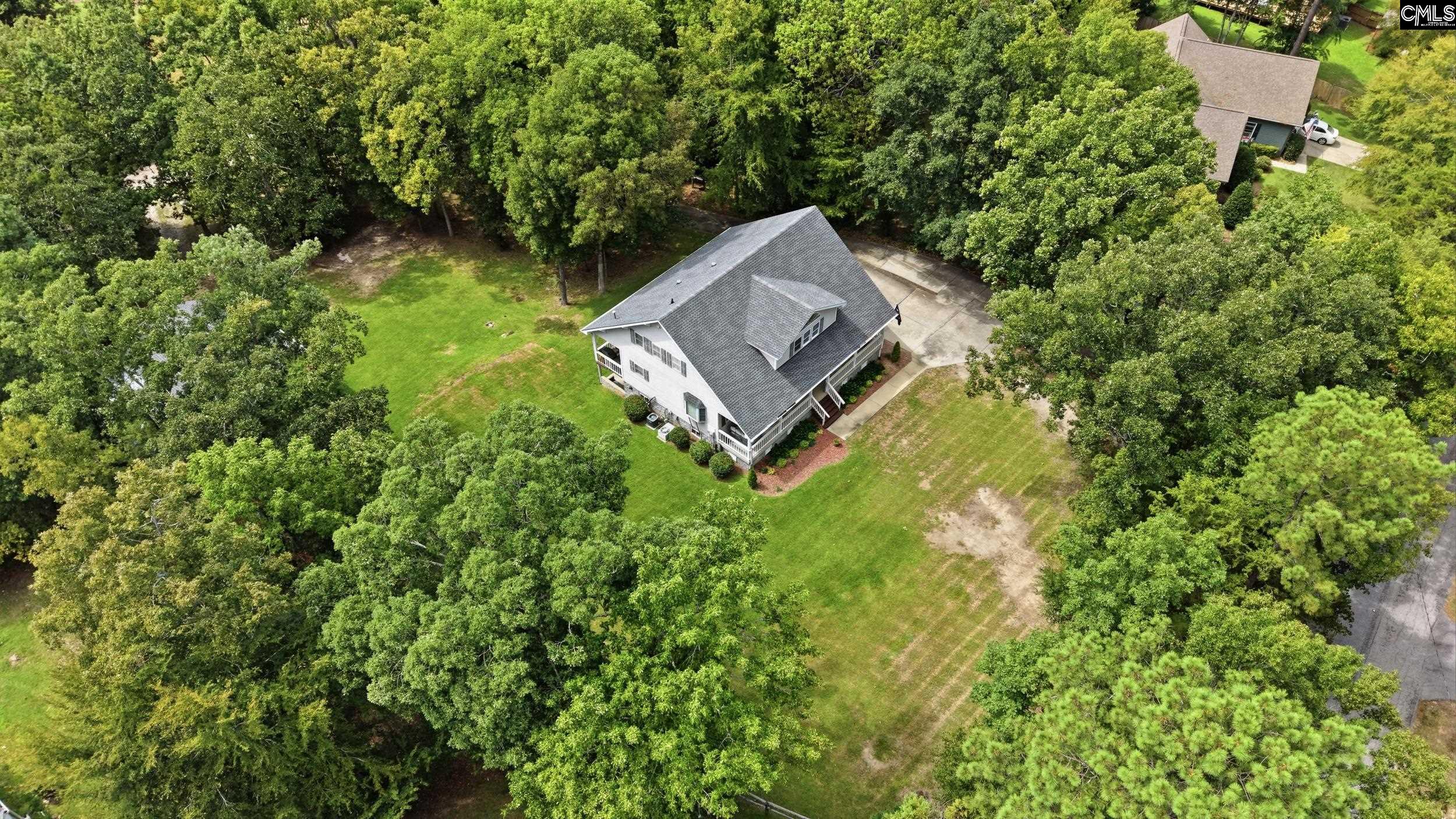 Aerial view of a white house with a wraparound porch in a large, tree-lined yard.