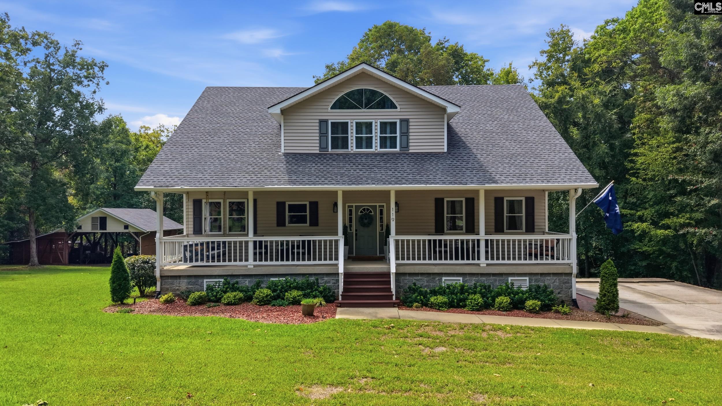 Two-story beige home with a wide covered front porch, upper dormer, and a green lawn.