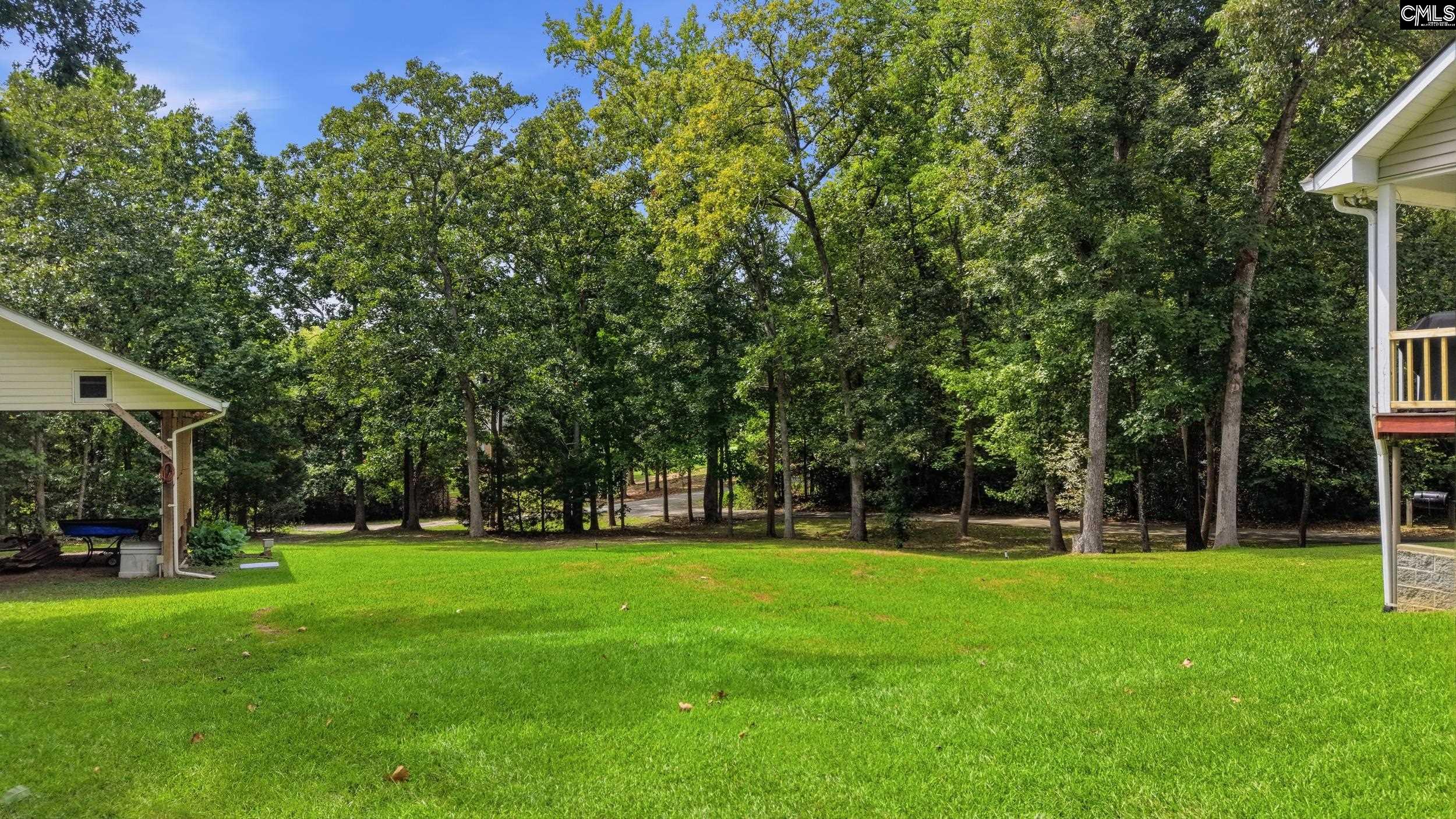 Backyard lawn bordered by mature trees, with parts of the home visible at the edges.
