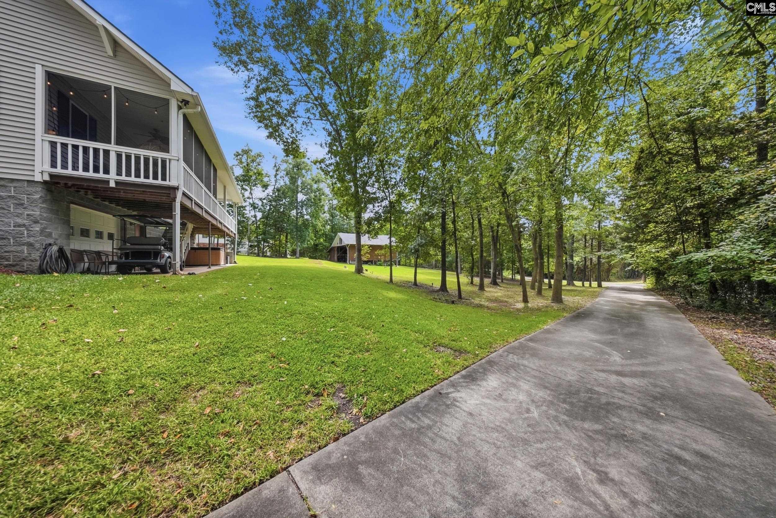 Home with a raised screened porch beside a curving driveway through a wooded yard.