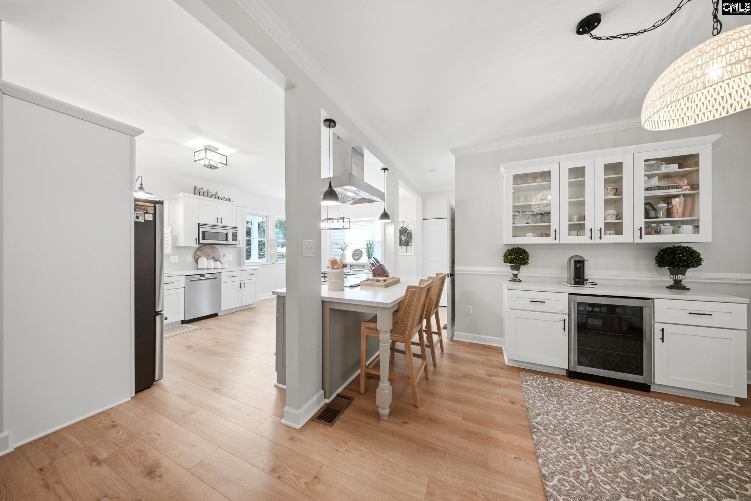 Open-plan kitchen with white cabinets, a wood-stool island, and a glass-front serving area.