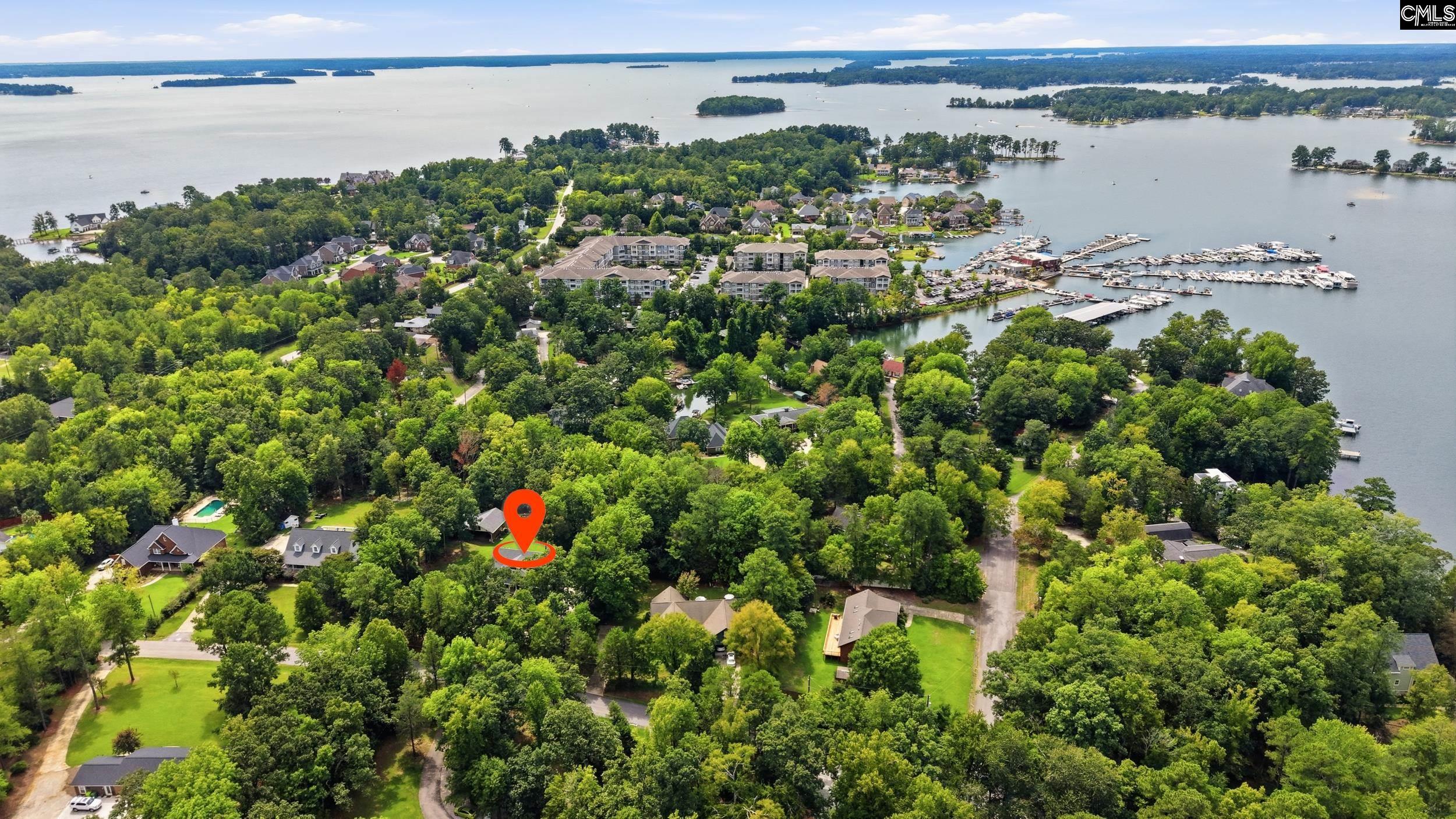 Aerial view of a wooded lakeside neighborhood, with a property marker and marina along the water.