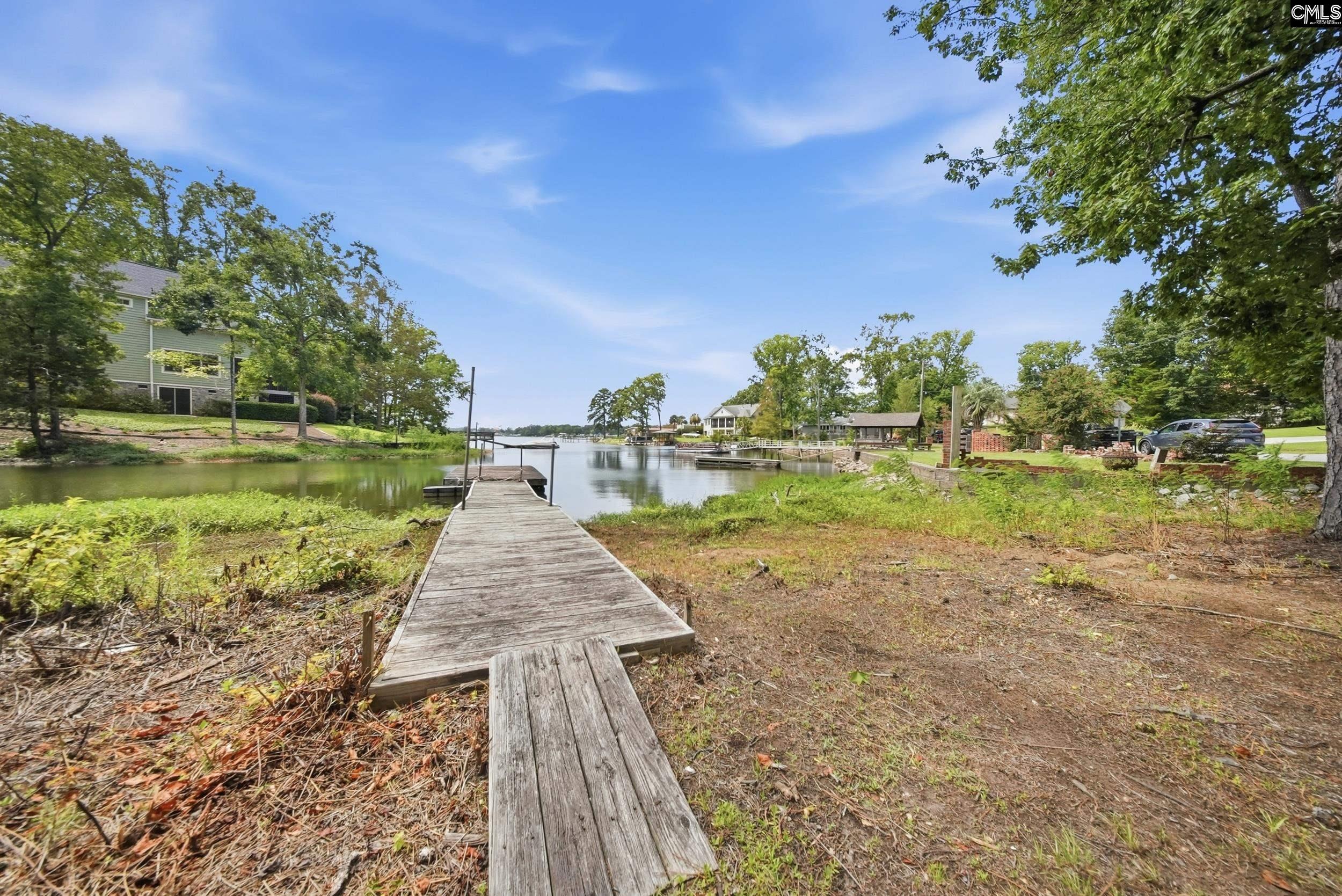 Waterfront dock extending into a calm channel, with homes and leafy trees along the banks.