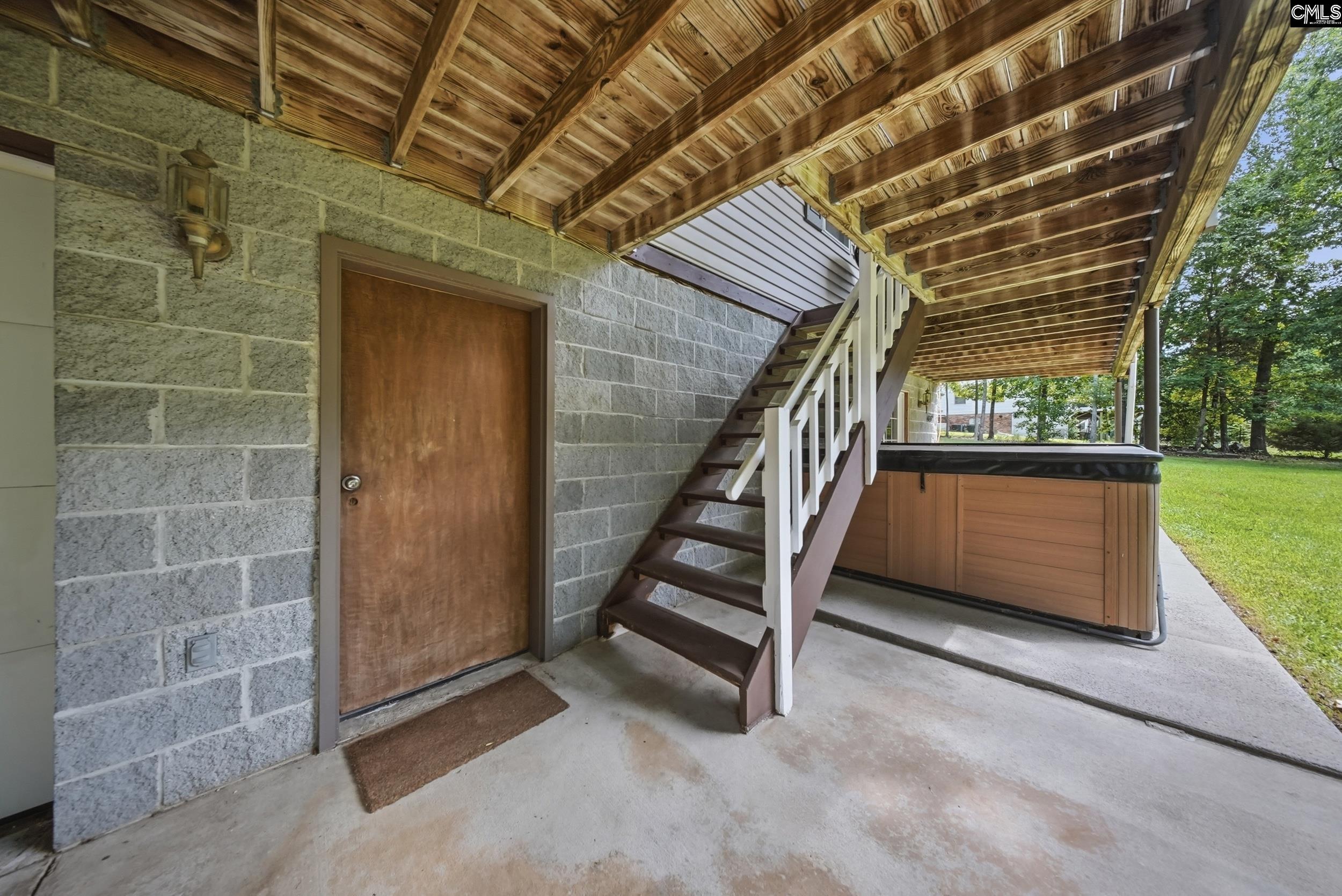 Covered patio with exposed timber ceiling, stairs, and a hot tub beside the yard.