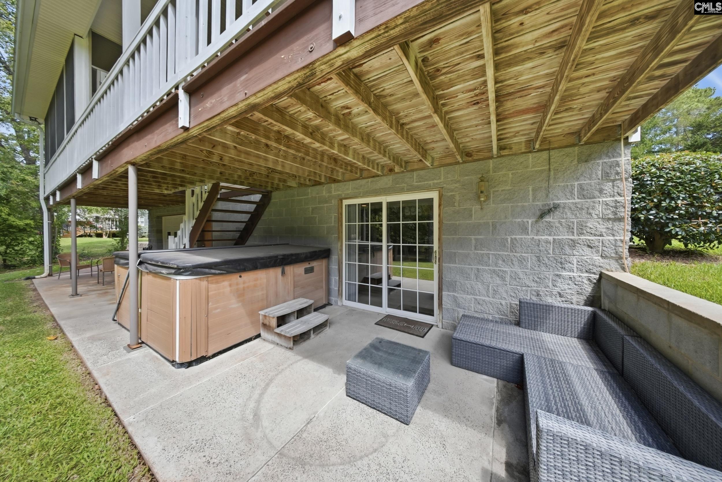 Covered patio with a hot tub and wicker seating beneath a raised wooden deck.