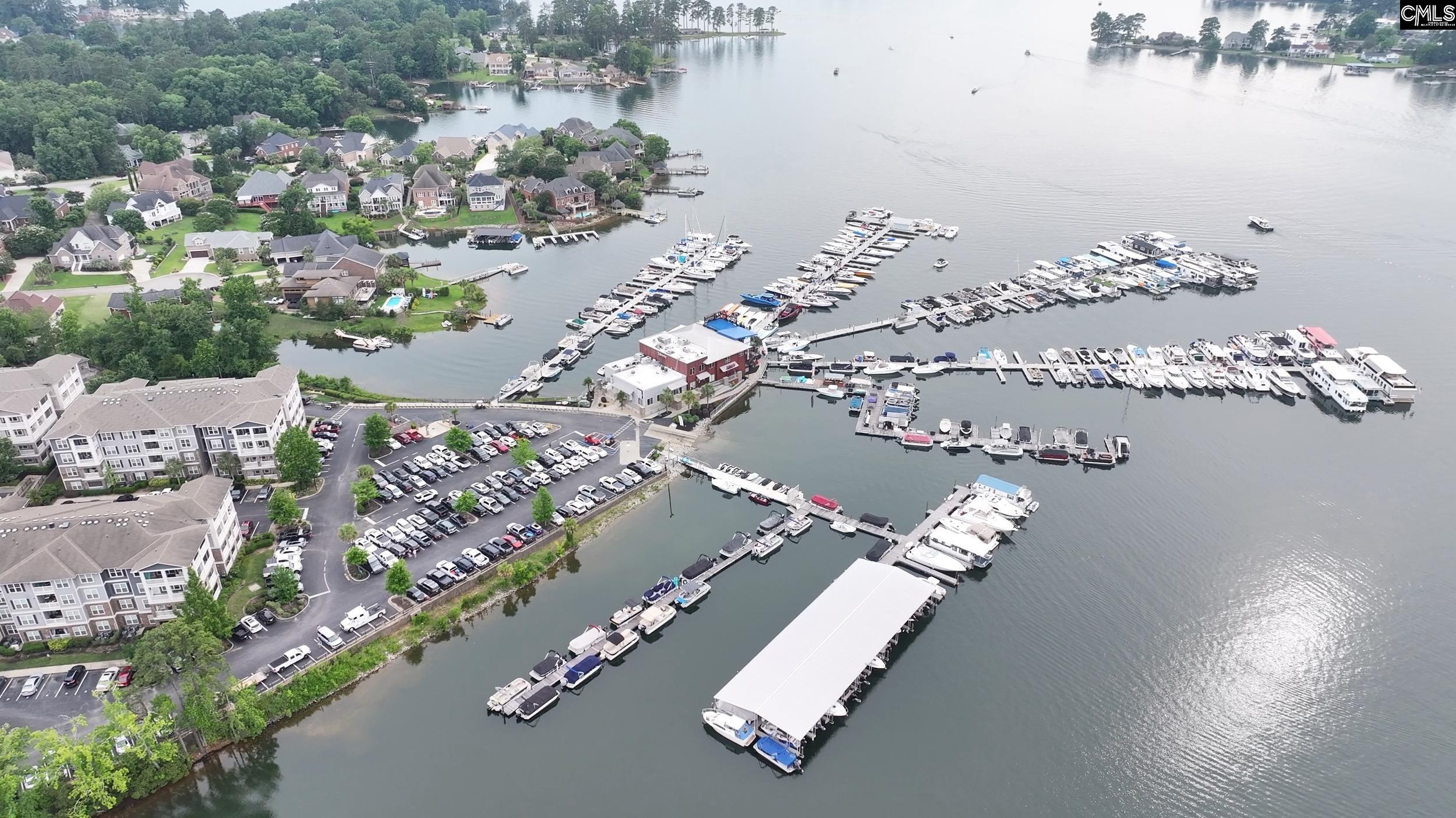 Aerial view of a lake marina with rows of boats, piers, waterfront homes, and apartment buildings.