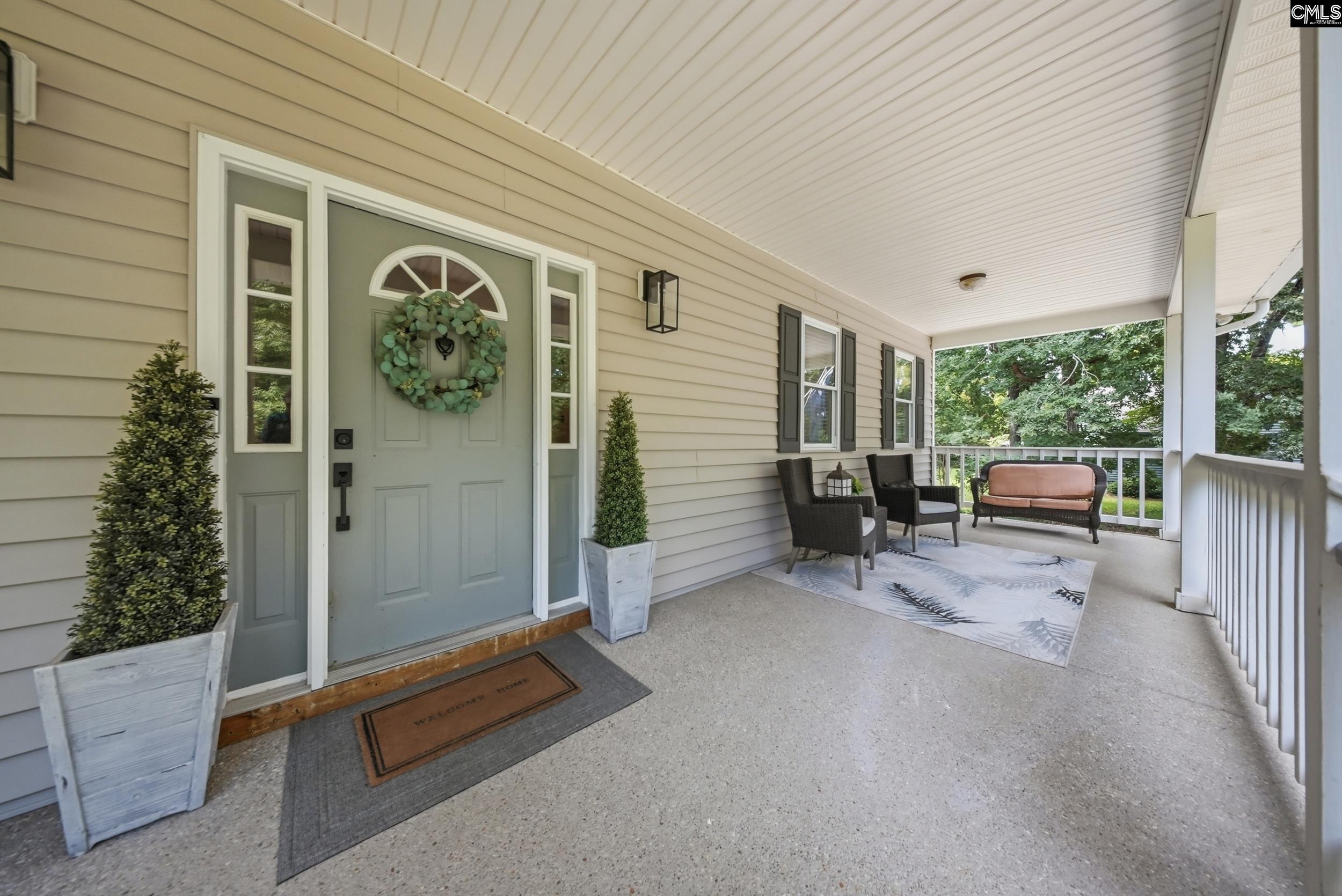 Covered front porch with a wreath-adorned entry door and seating beside the white railing.