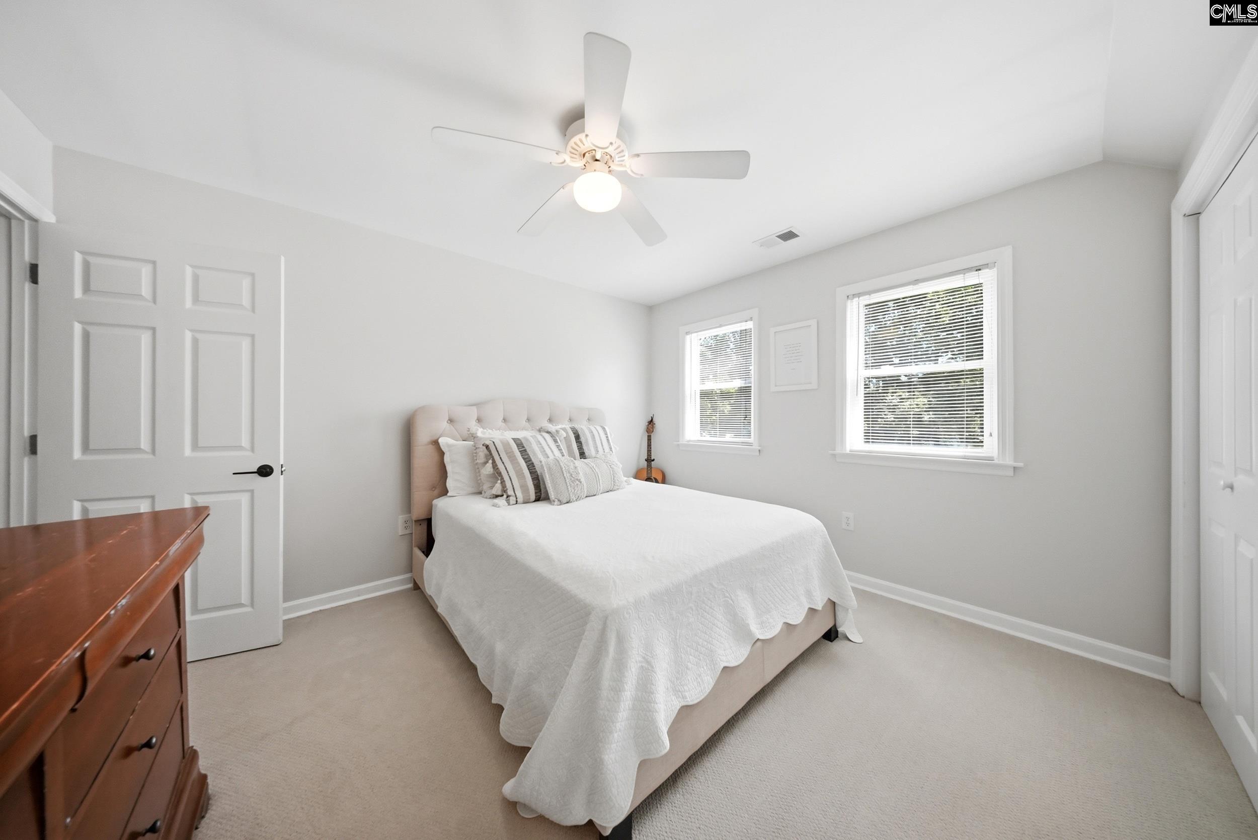 Furnished bedroom with a white bed, striped pillows, two windows, and a ceiling fan.