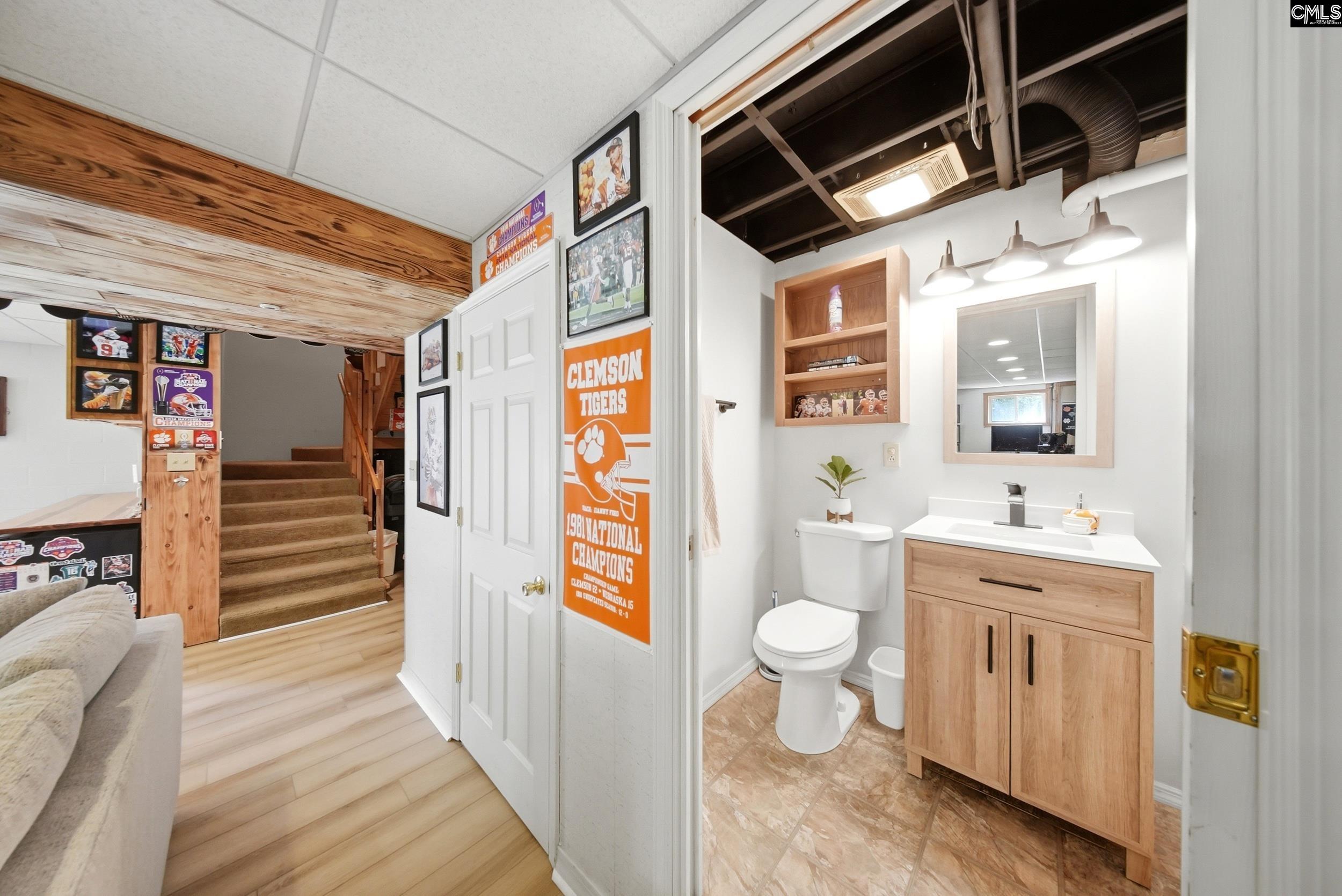 Basement bathroom with a wood vanity and exposed ceiling beside a staircase and Clemson Tigers decor.