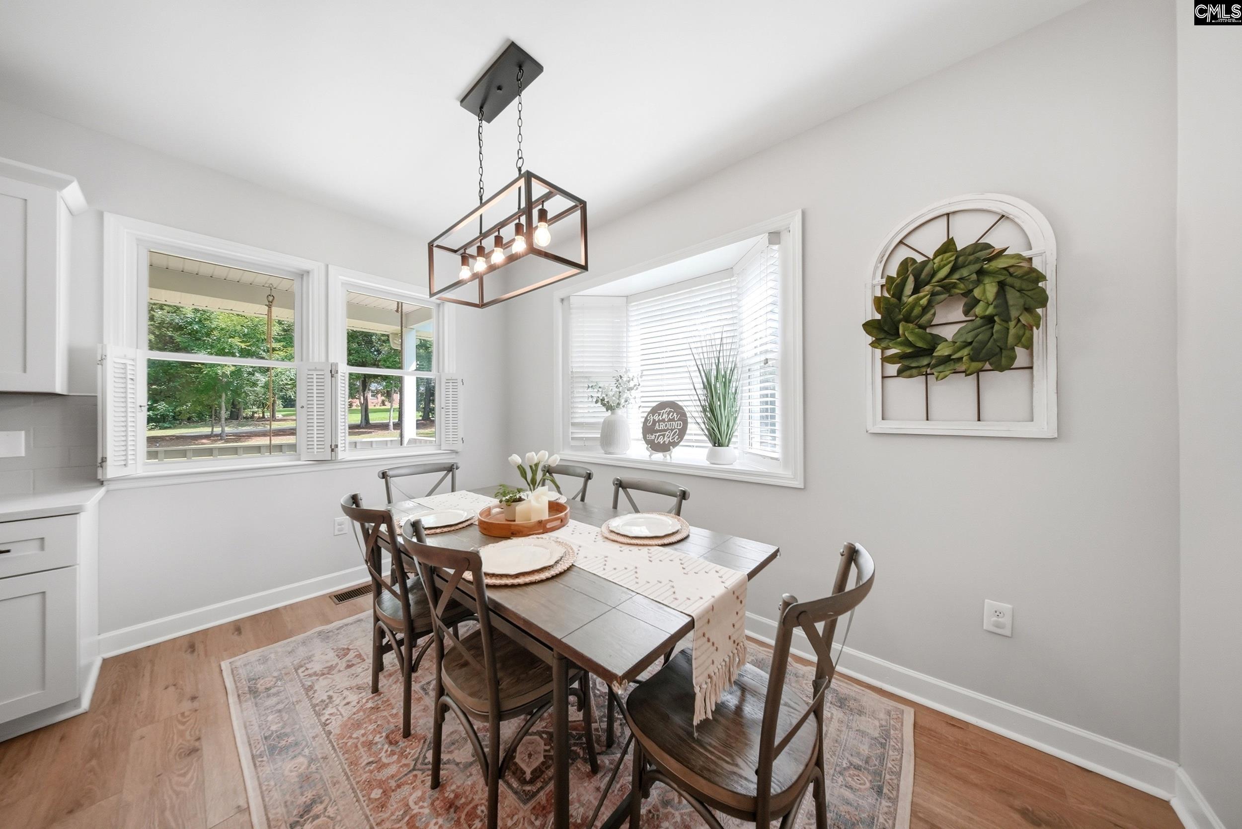 Dining area with a dark wood table, patterned rug, large windows, and geometric pendant light.