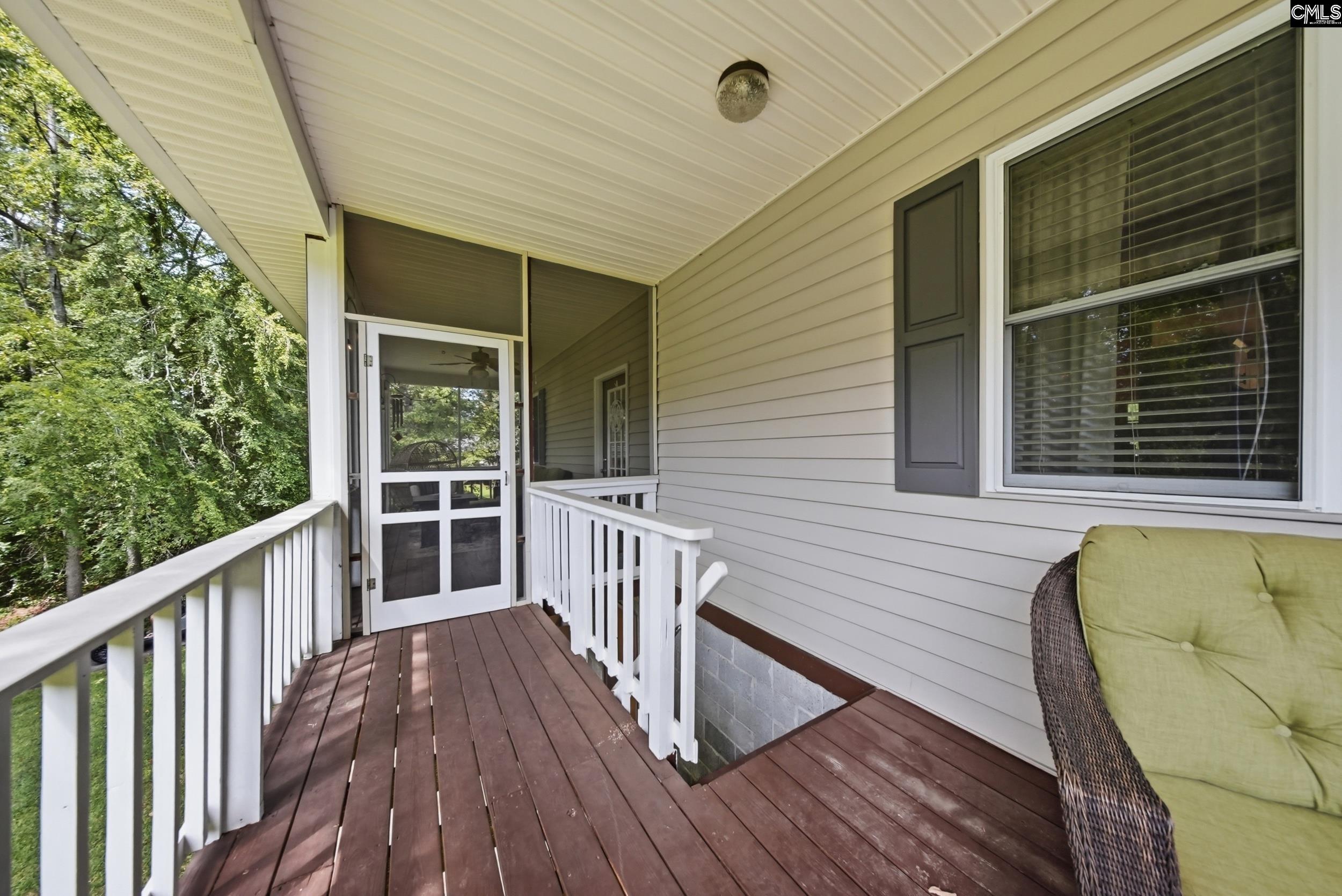 Covered front porch with white railings, wooden decking, and a wicker chair beside the entrance.