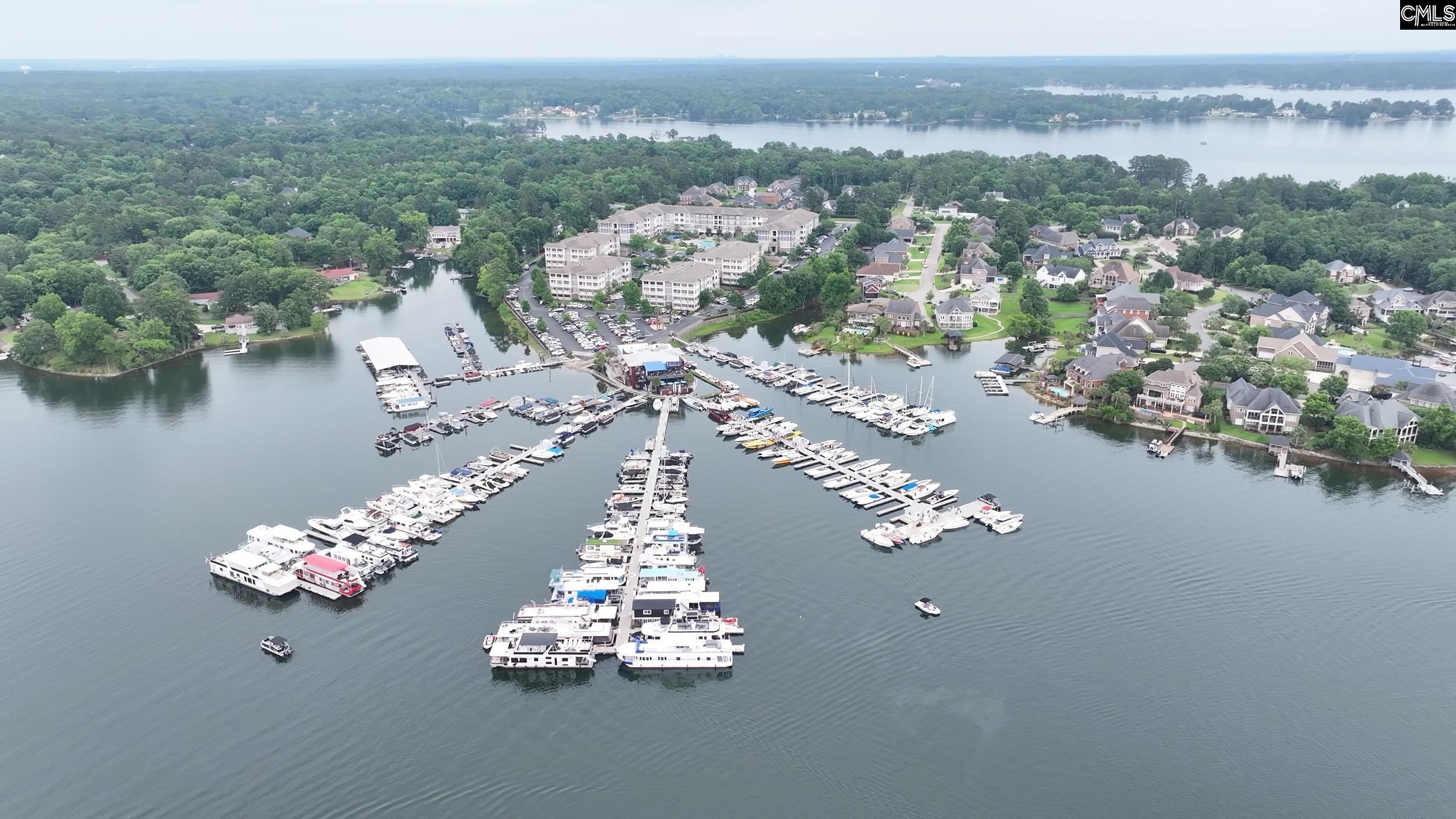 Aerial view of a marina with rows of boats and lakeside homes along a wooded shoreline.