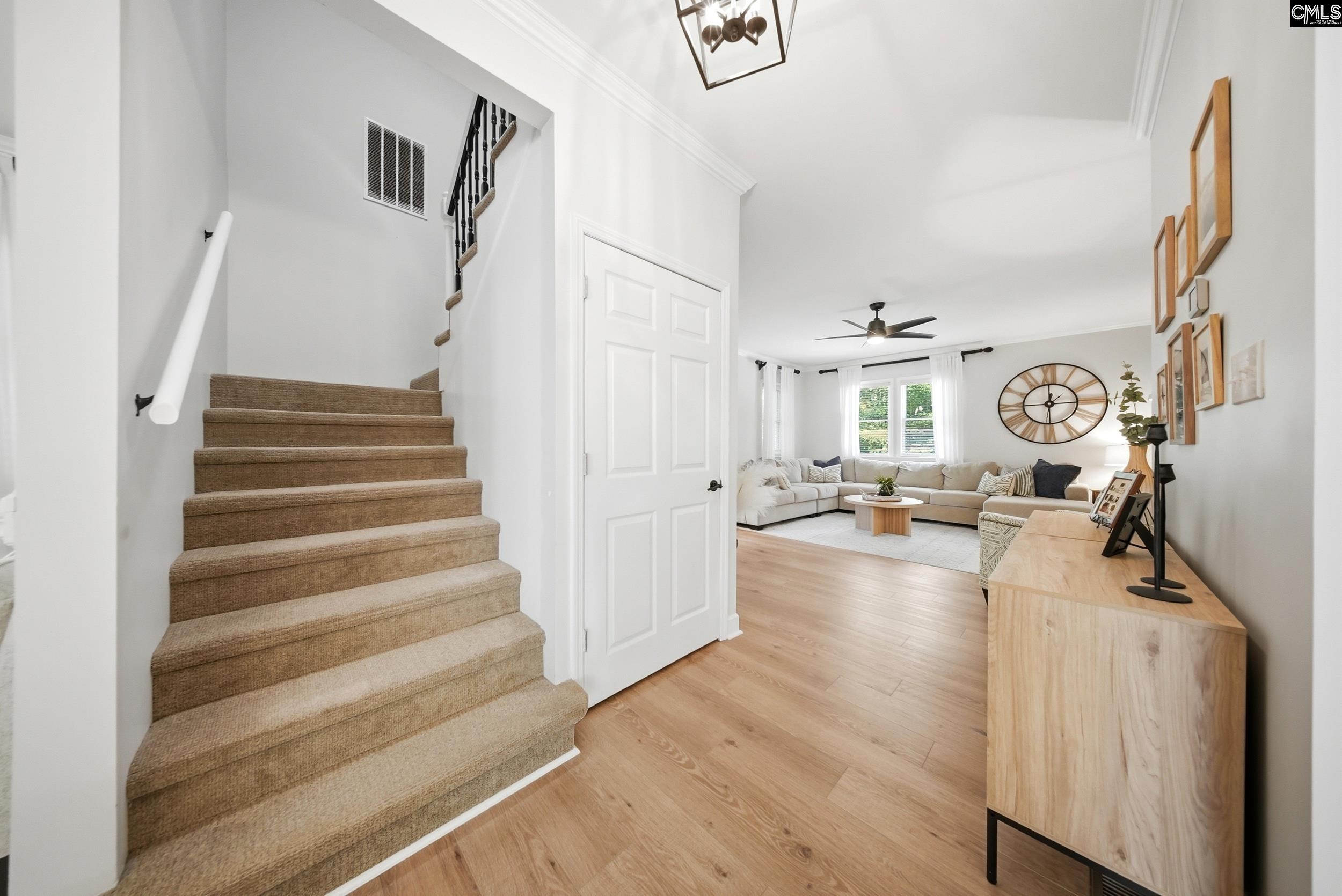 Carpeted staircase opens onto a bright living room with a sectional sofa and wood floors.