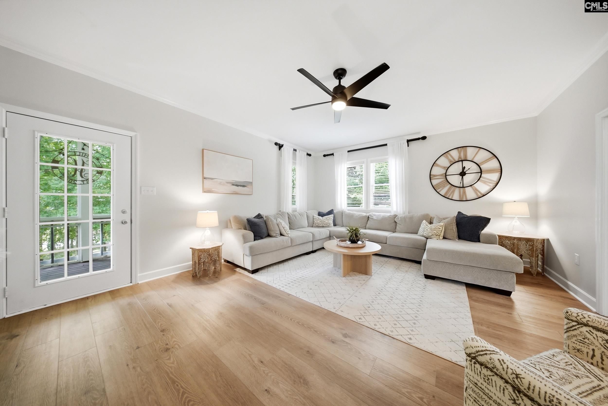 Staged living room with a light gray sectional, patterned rug, and oversized wall clock.