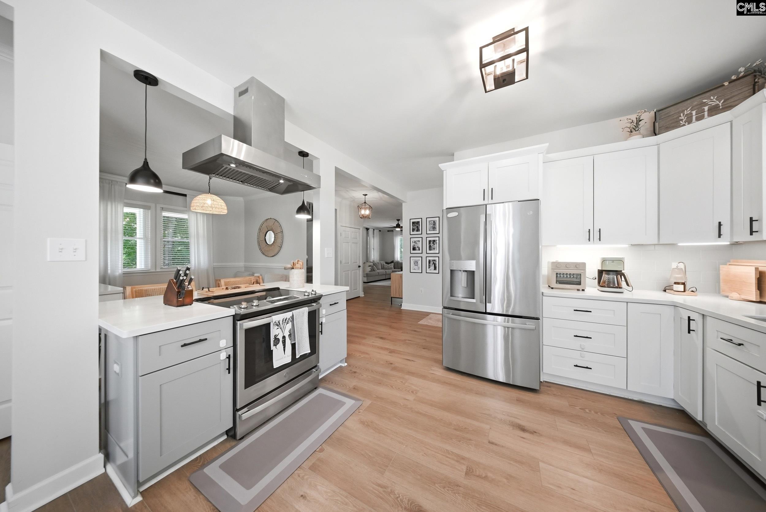 Bright white kitchen with stainless steel appliances, a large cooktop island, and light wood floors.