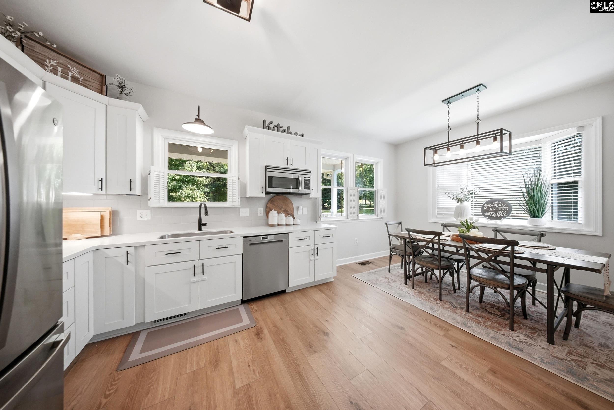 Bright white kitchen opens to a dining area with a long table and large windows.