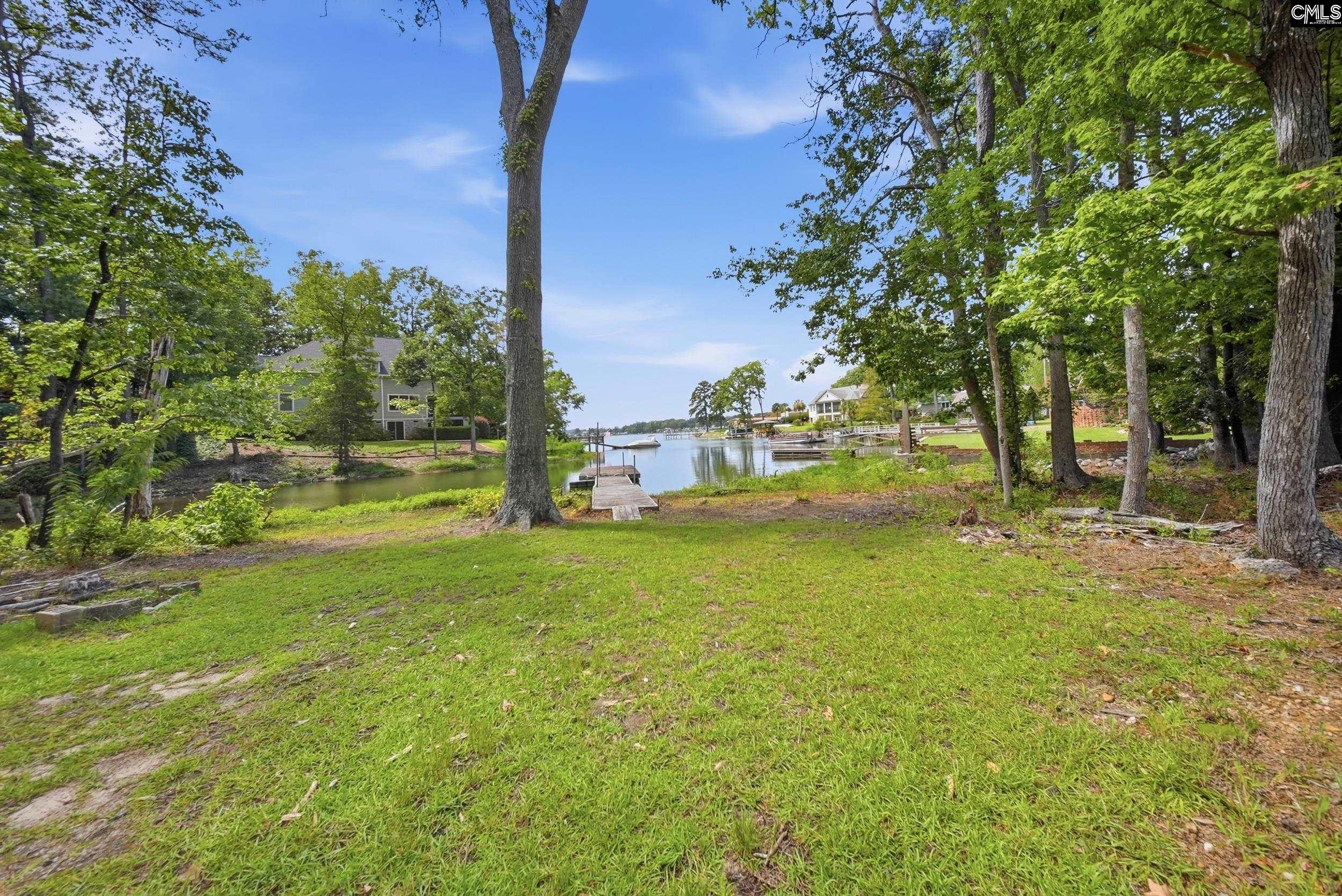 Tree-lined waterfront yard with a wooden dock extending into a calm inlet.