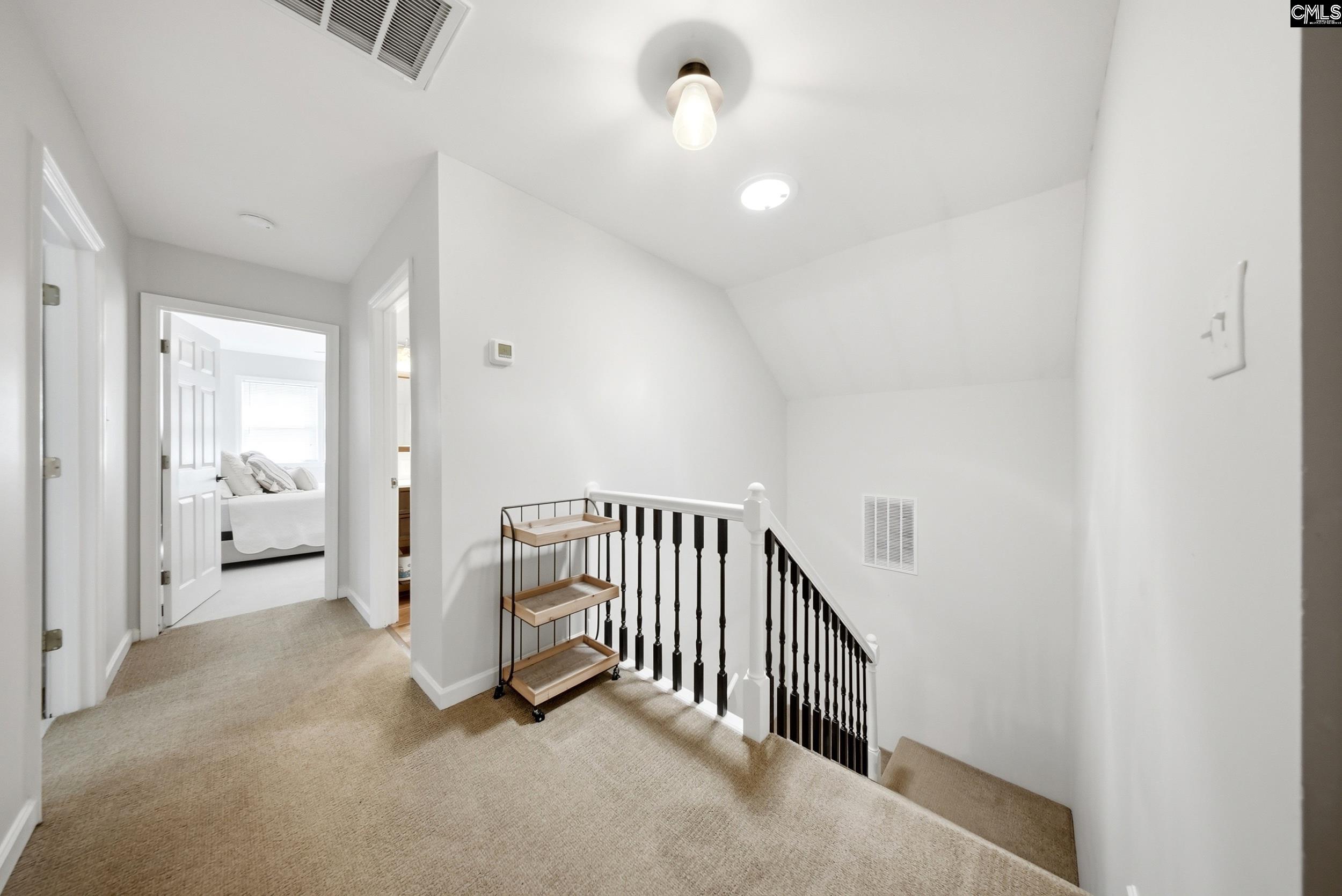 Upstairs landing with beige carpet, black-and-white stair railing, and an open doorway to a bedroom.