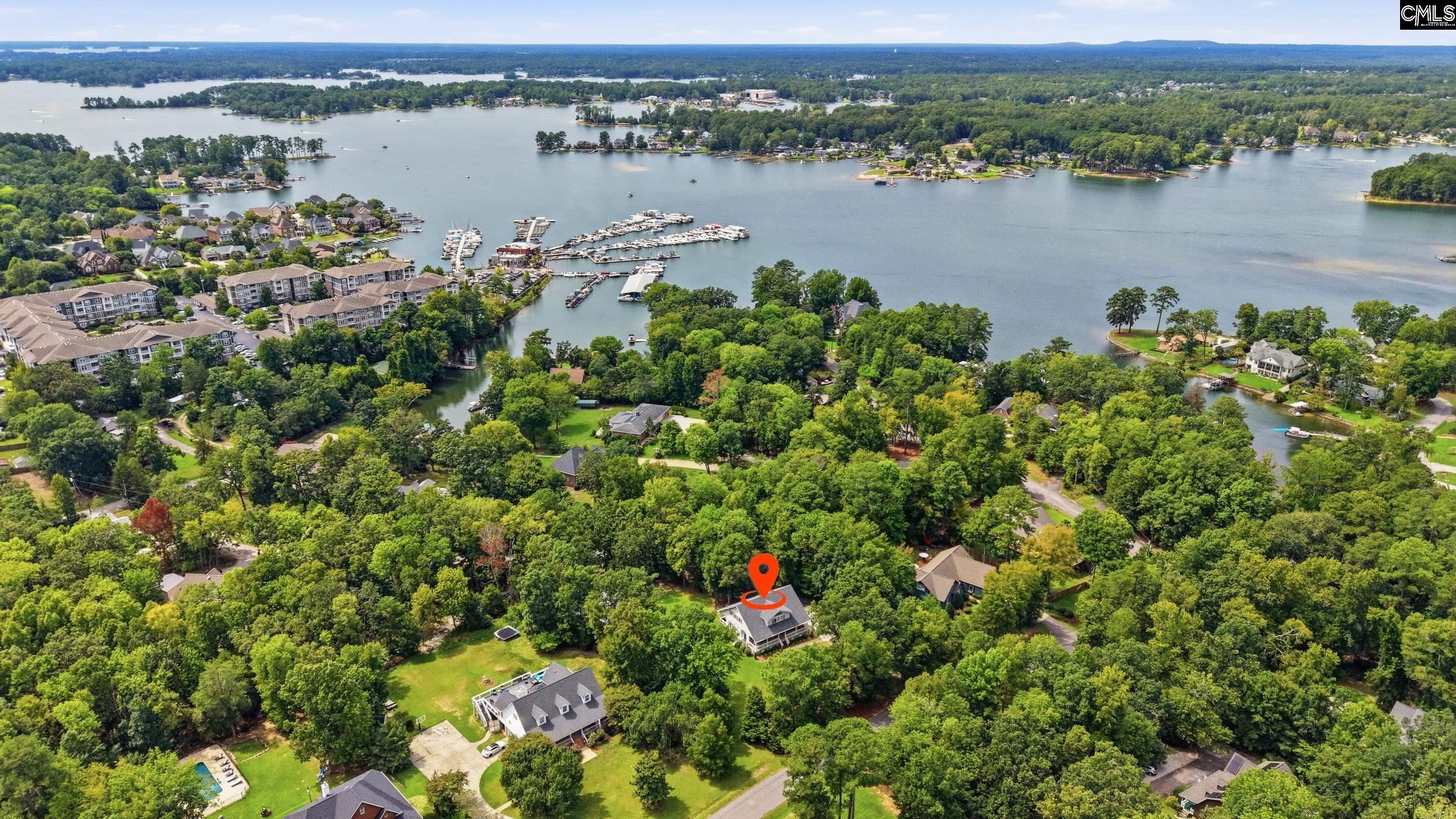 Aerial view of the marked home amid trees, with a lake and marina in the distance.