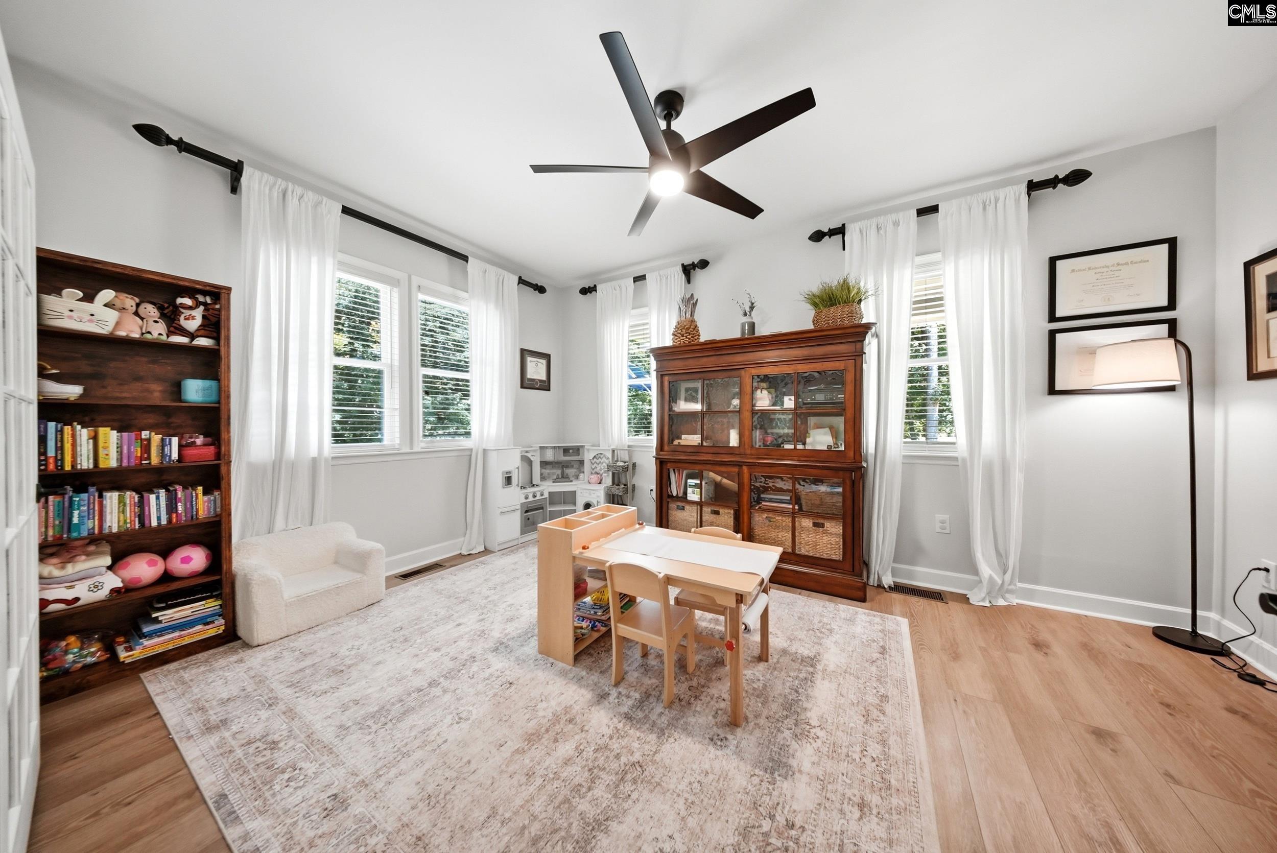 Playroom with a child-sized table, toy shelves, wooden display cabinet, and tall curtained windows.