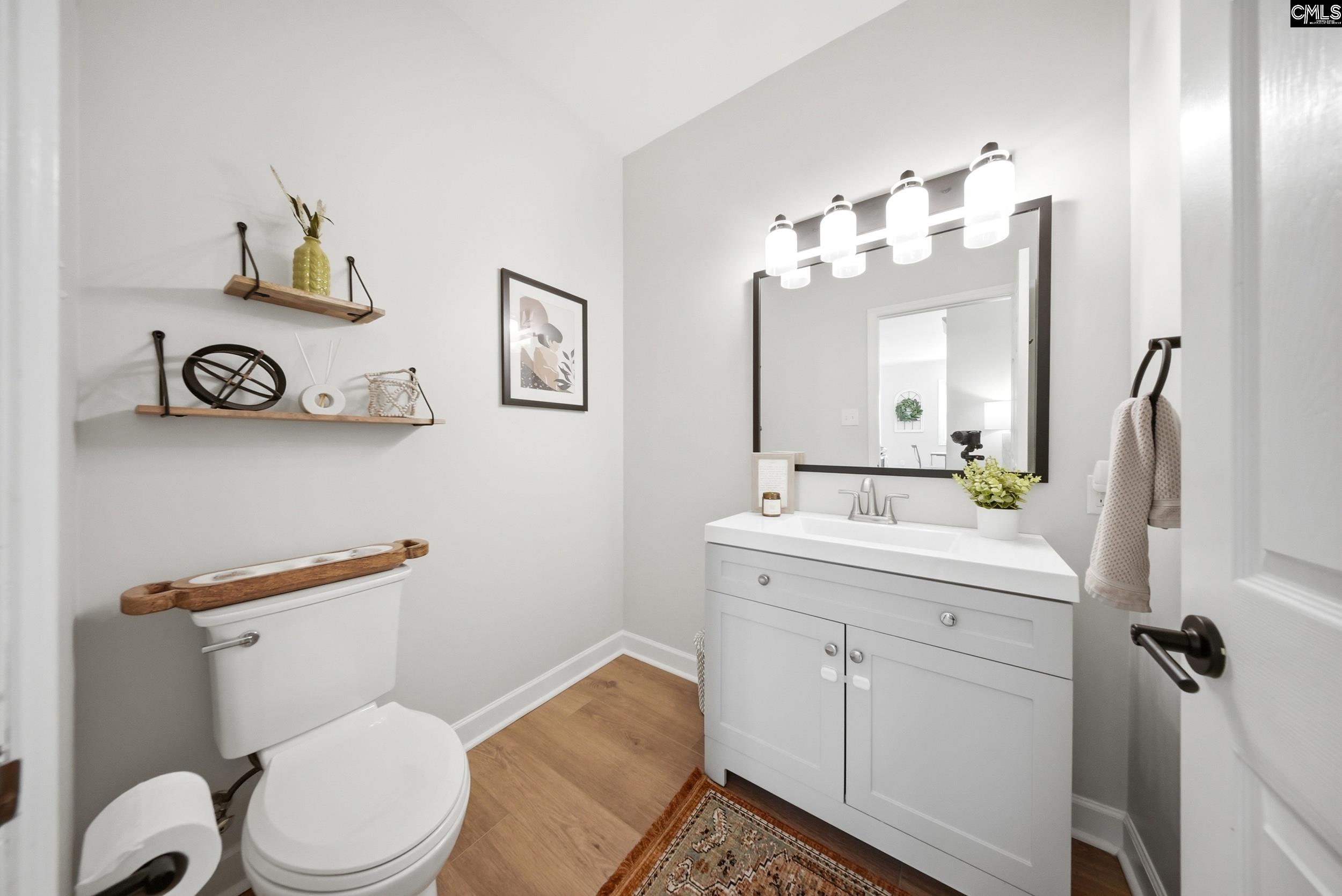 Staged bathroom with a white vanity, large mirror, floating shelves, and wood-look flooring.